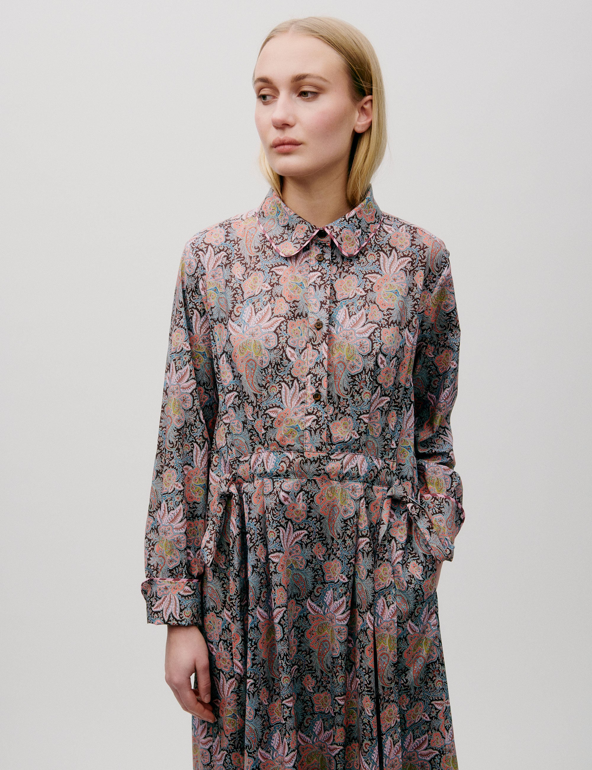 Woman in long dress with pink and blue flower paisley pattern, buttons, long sleeves and pockets