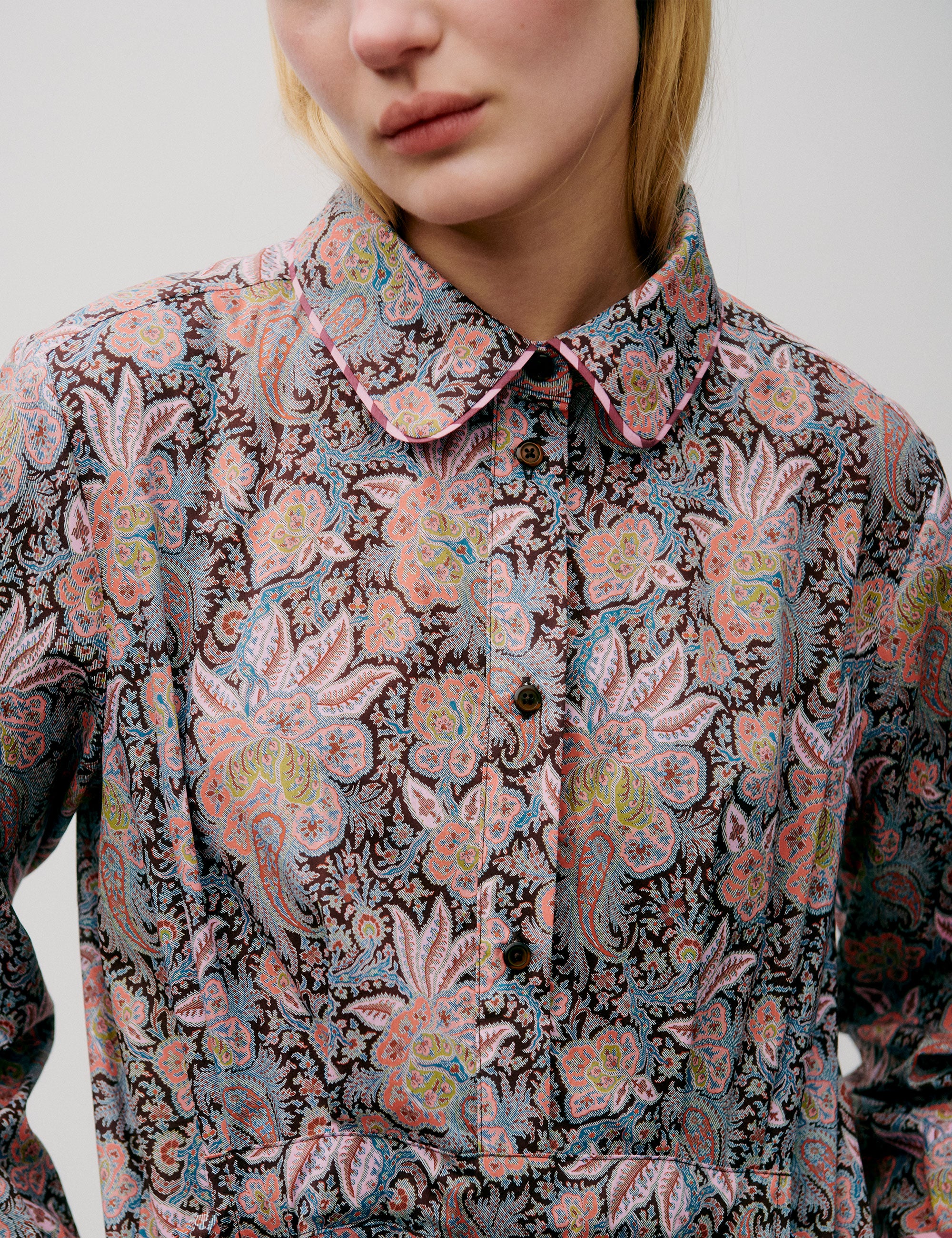 Woman in long dress with pink and blue flower paisley pattern, buttons, long sleeves and pockets