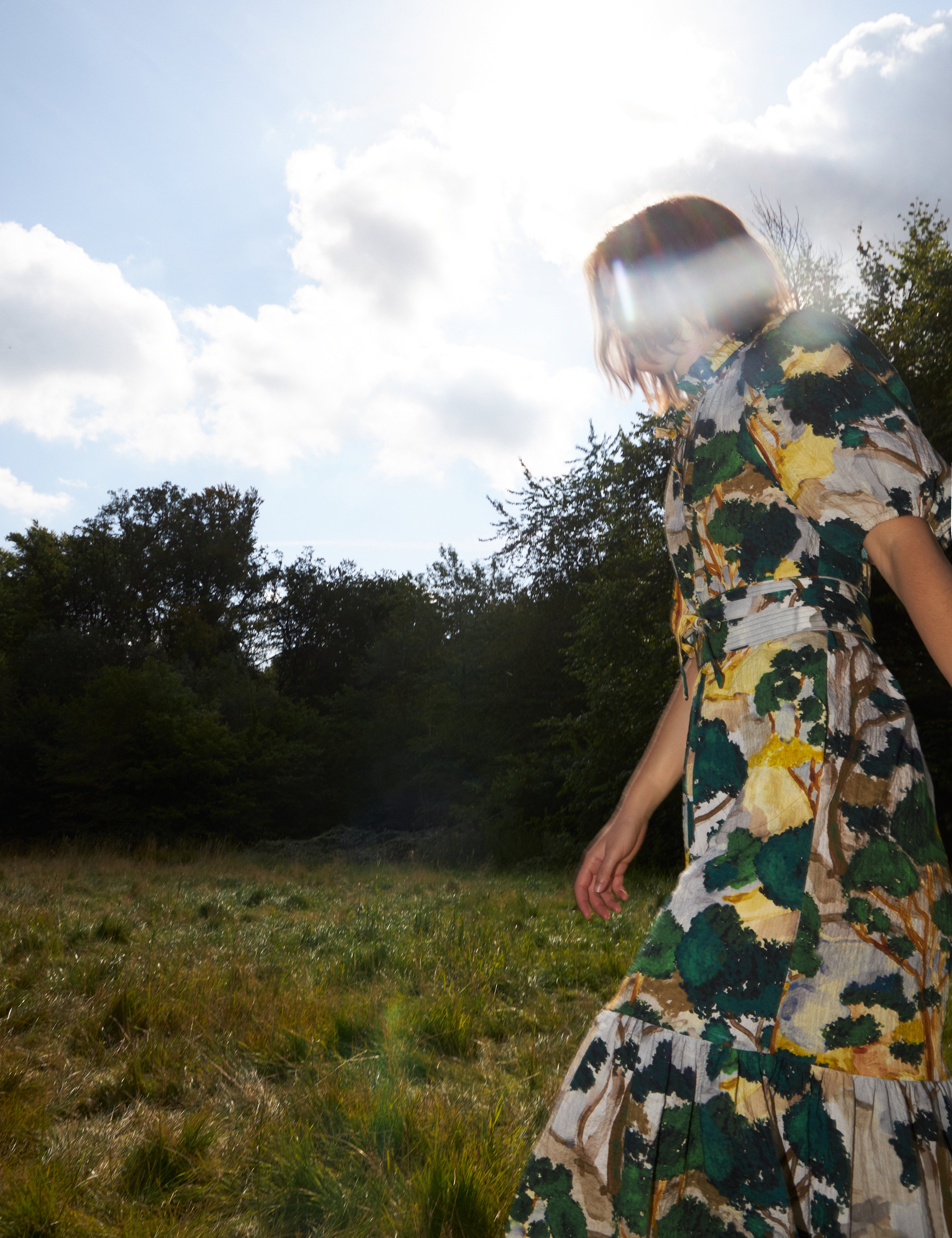 Woman in maxi dress with artistic green yellow and white print, short puff sleeves, belt and buttoned collar