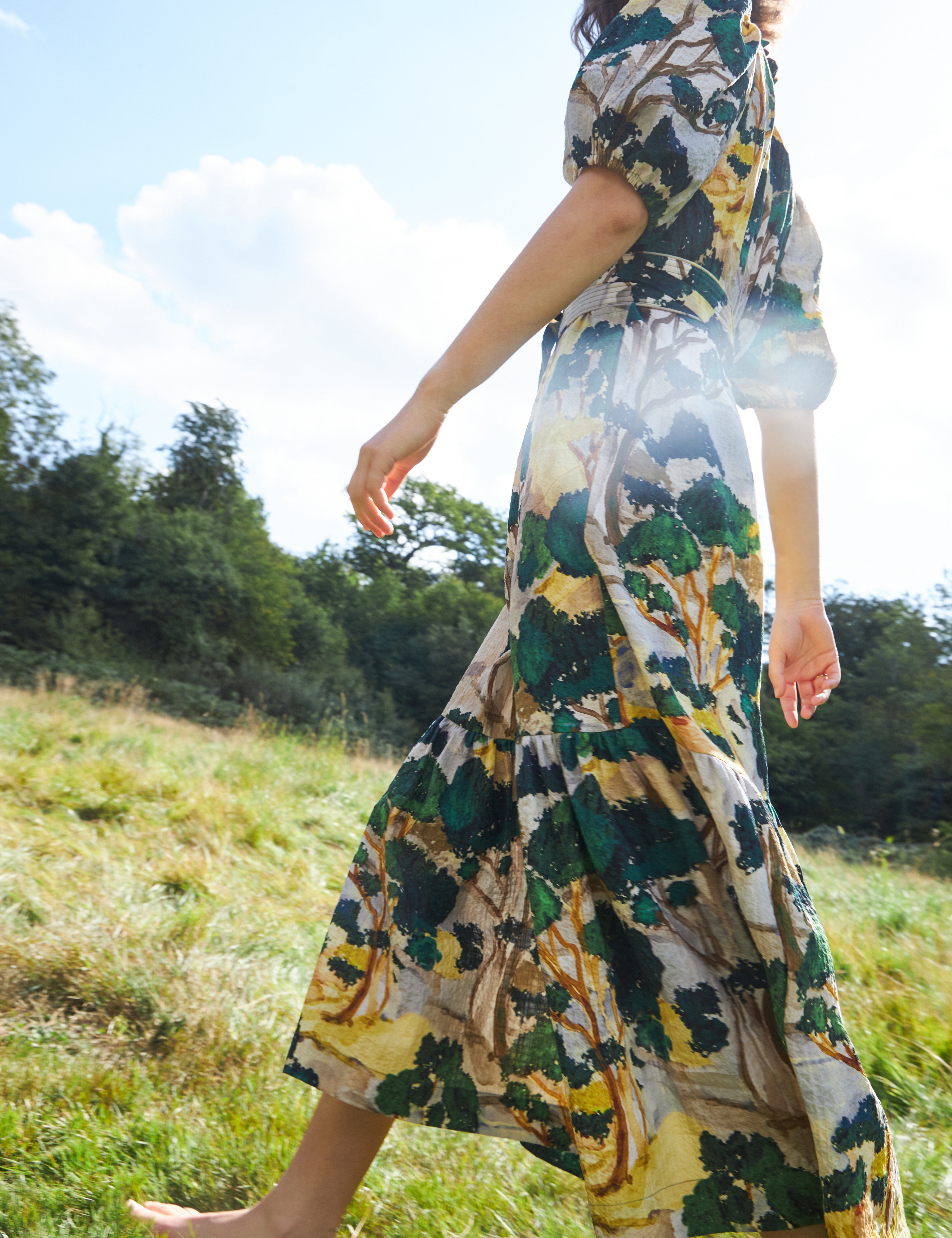 Woman in maxi dress with artistic green yellow and white print, short puff sleeves, belt and buttoned collar
