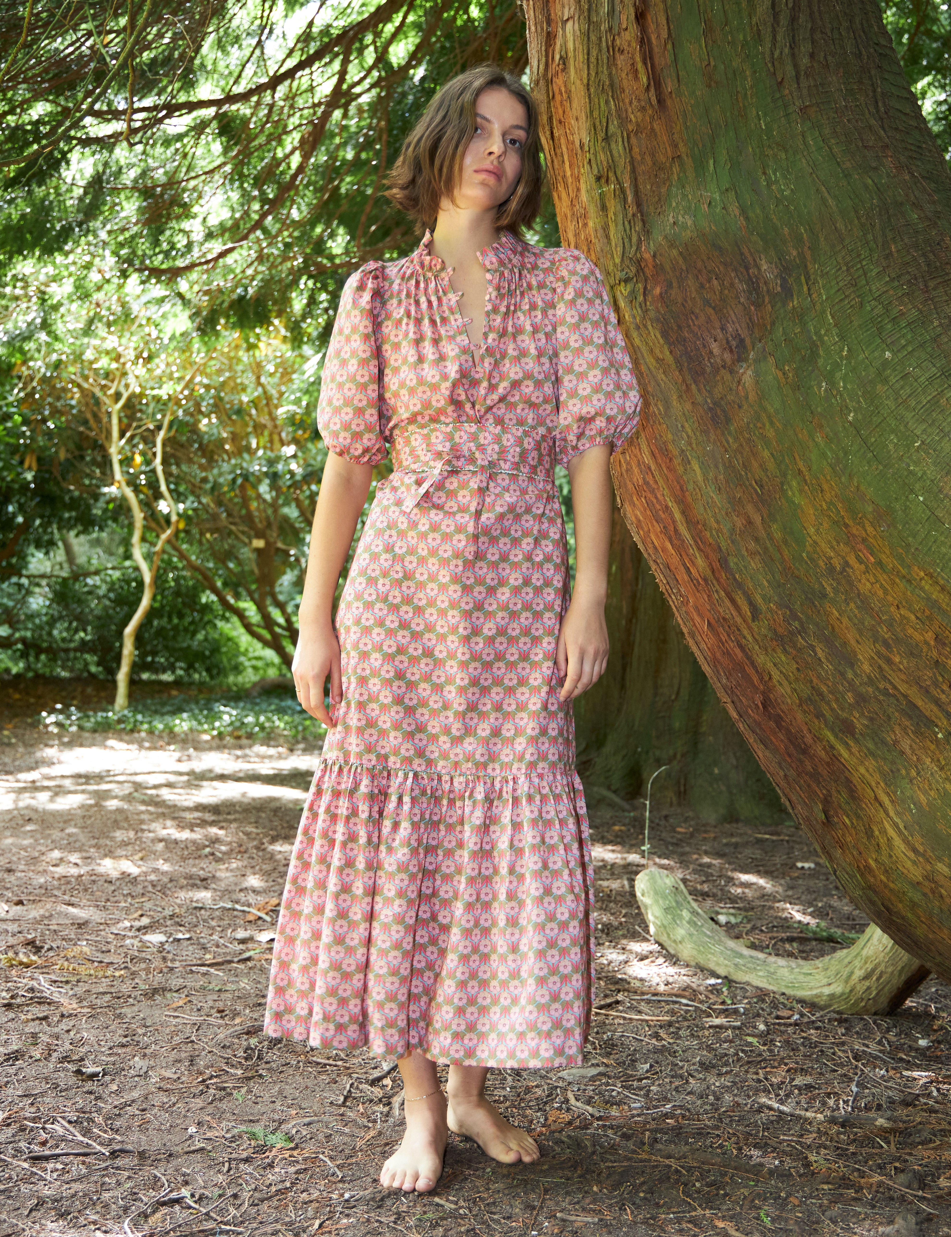 Woman in maxi dress with pink flower print, short puff sleeves, belt and buttoned collar
