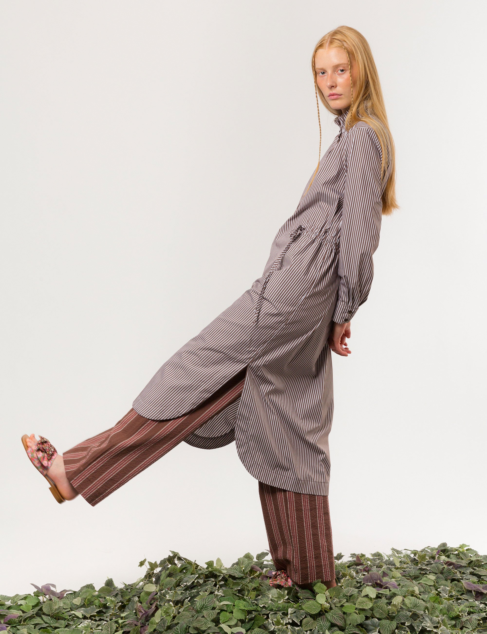 Woman in liberty cotton brown and white striped midi dress with long sleeves and ruffled collar and brown striped pants