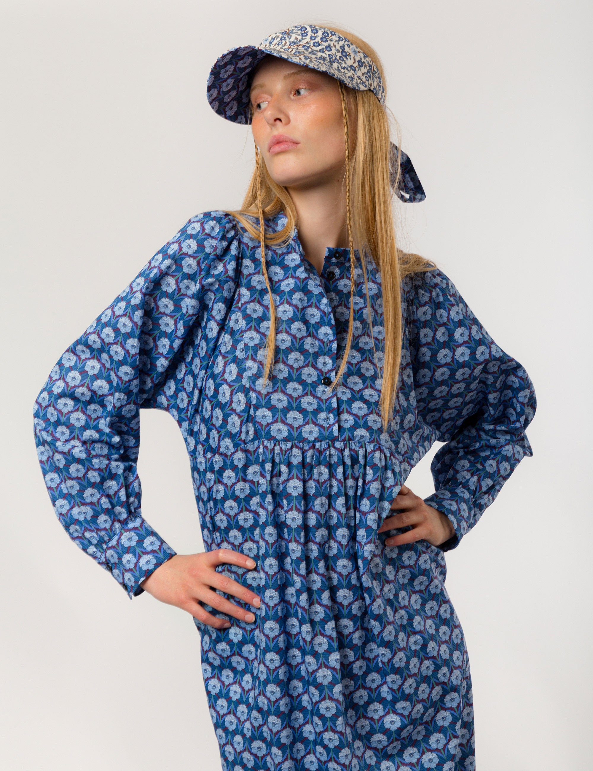 Woman in blue floral patterned dress with long sleeves and sun shade cap with blue and white flower pattern