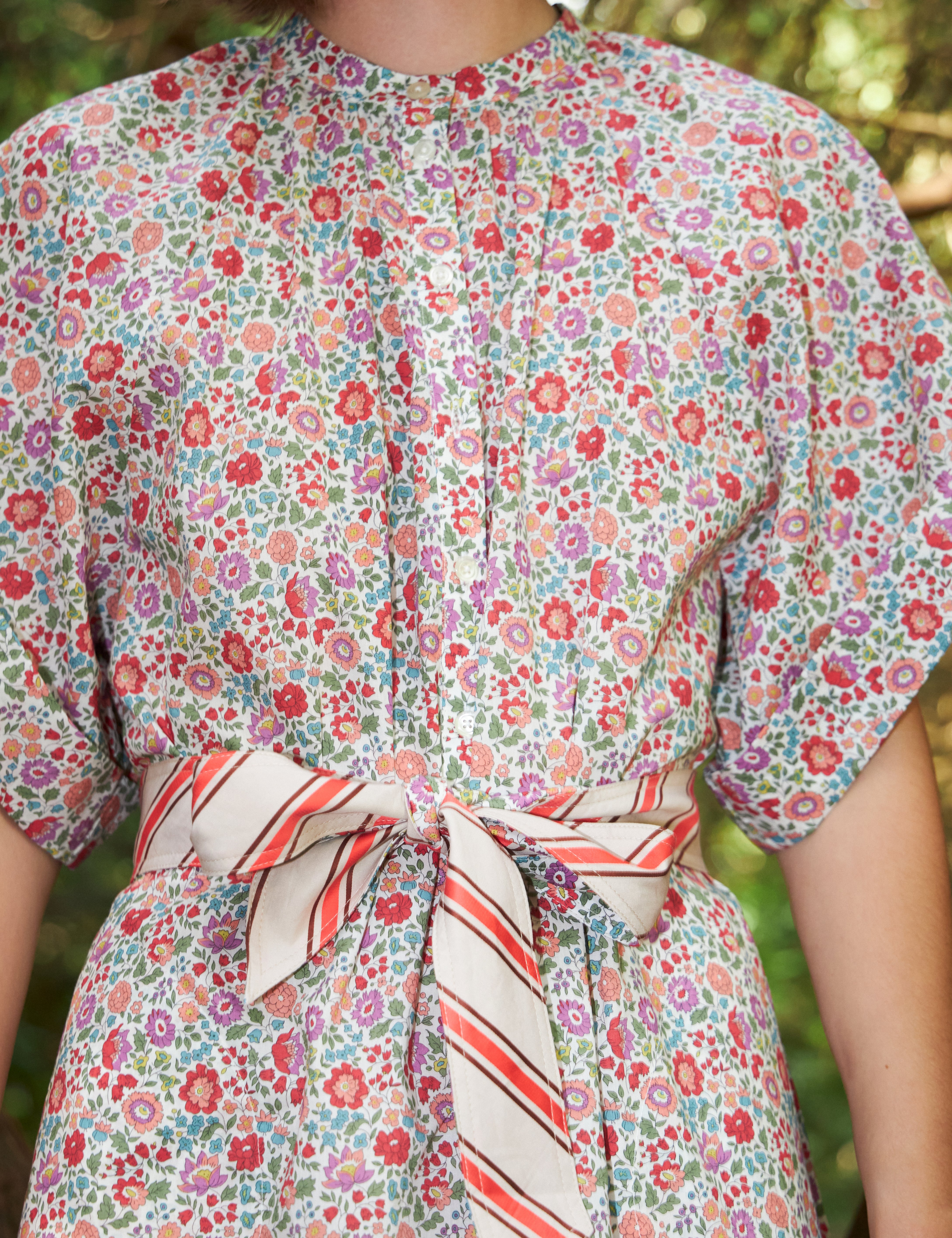 Woman in multi-colored pink an red floral patterned kaftan dress with kimono sleeves and red and white striped cotton belt