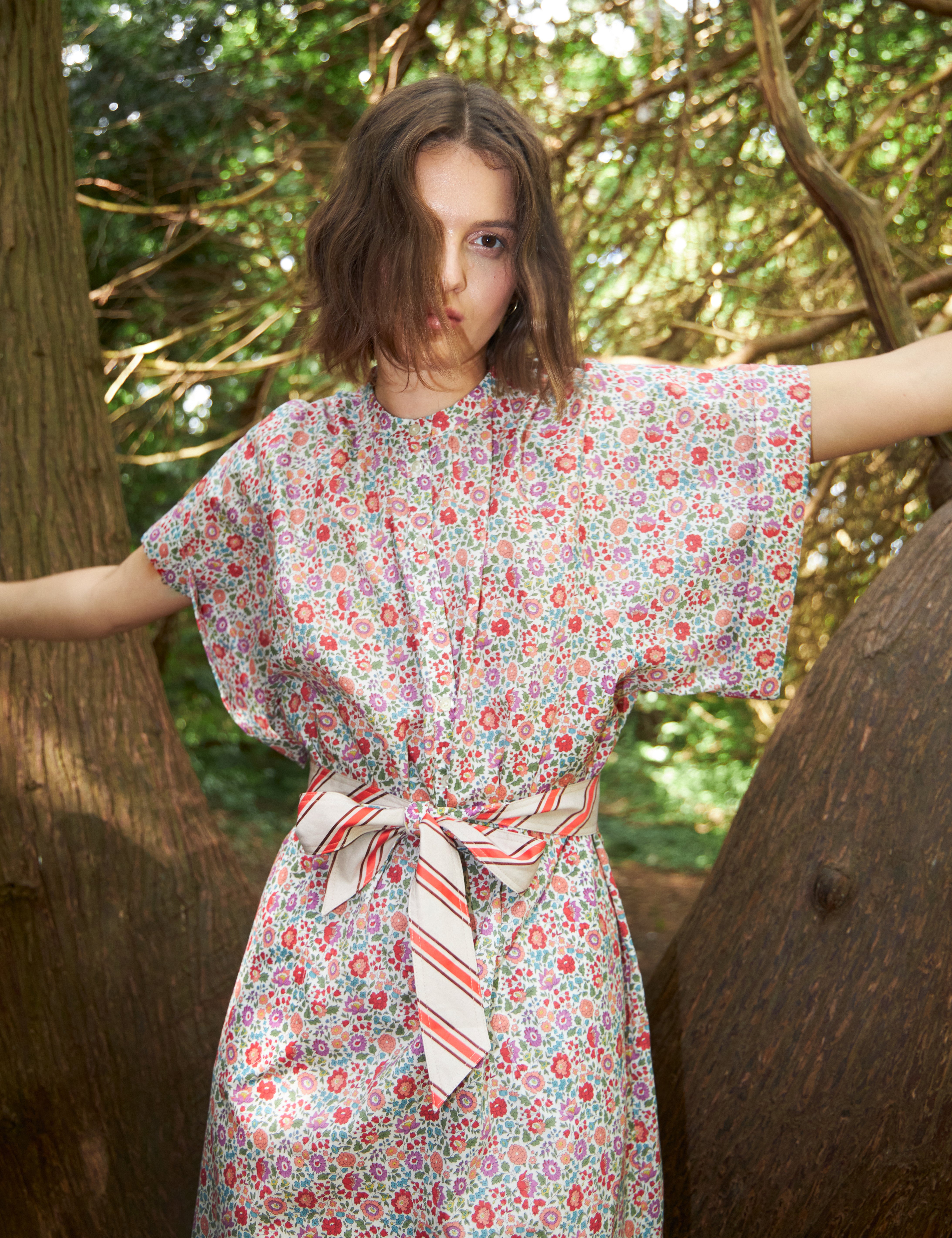 Woman in multi-colored pink an red floral patterned dress with kimono sleeves and red and white striped cotton belt