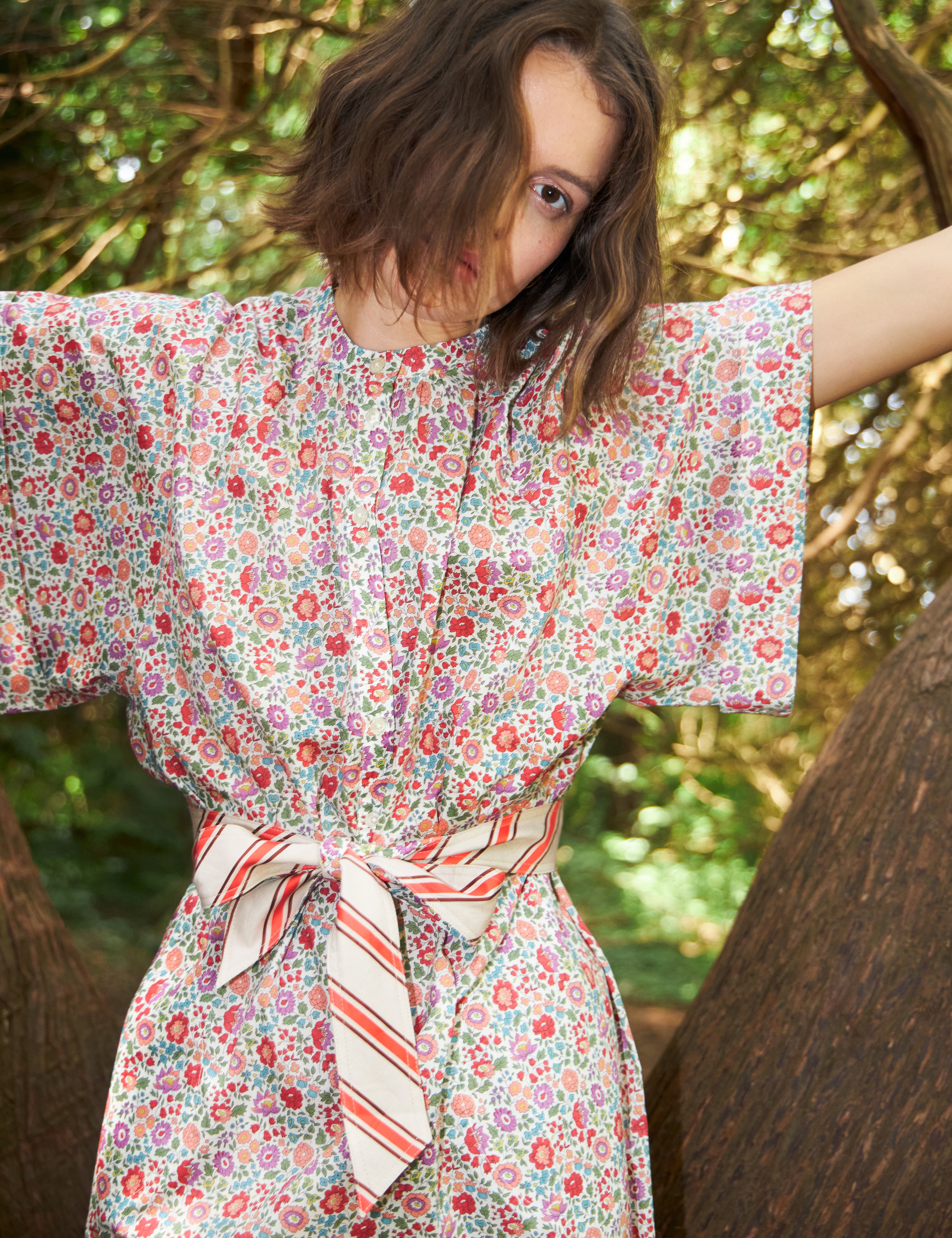 Woman in multi-colored pink an red floral patterned dress with kimono sleeves and red and white striped cotton belt