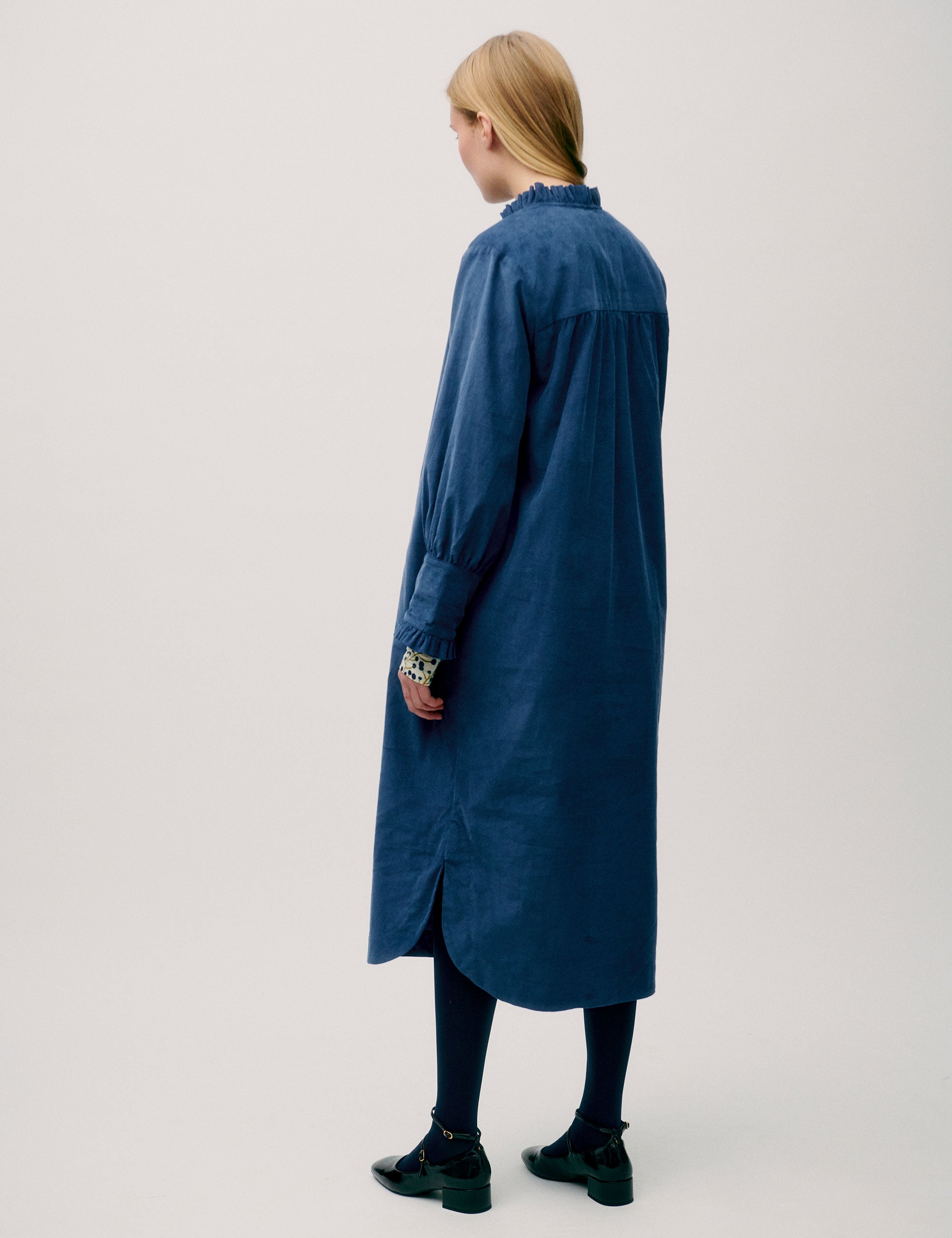 Woman wearing a loose-fitting blue corduroy shirt dress with ruffle detail and floral inner cuffs