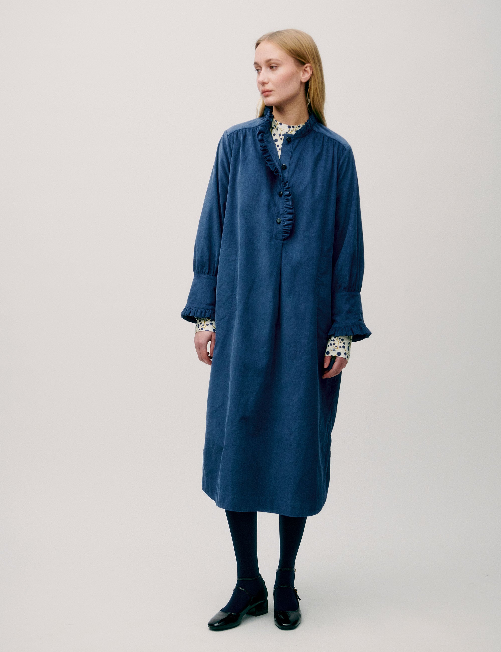 Woman wearing a loose-fitting blue corduroy shirt dress with ruffle detail and floral inner cuffs