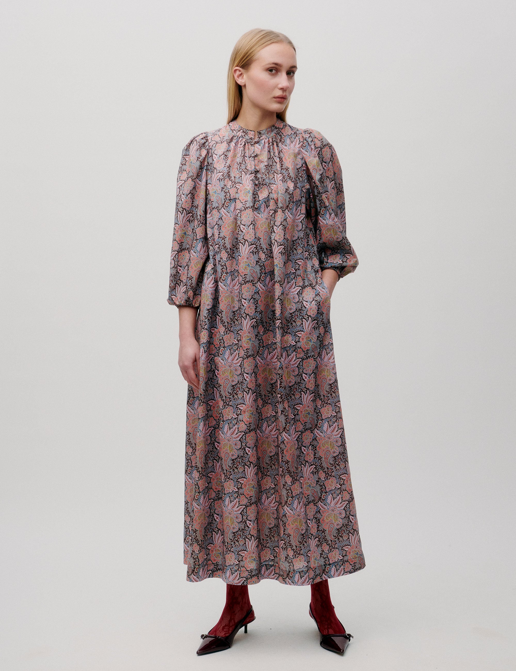 Woman wearing a long pink patterned dress with puff sleeves and gathered neckline