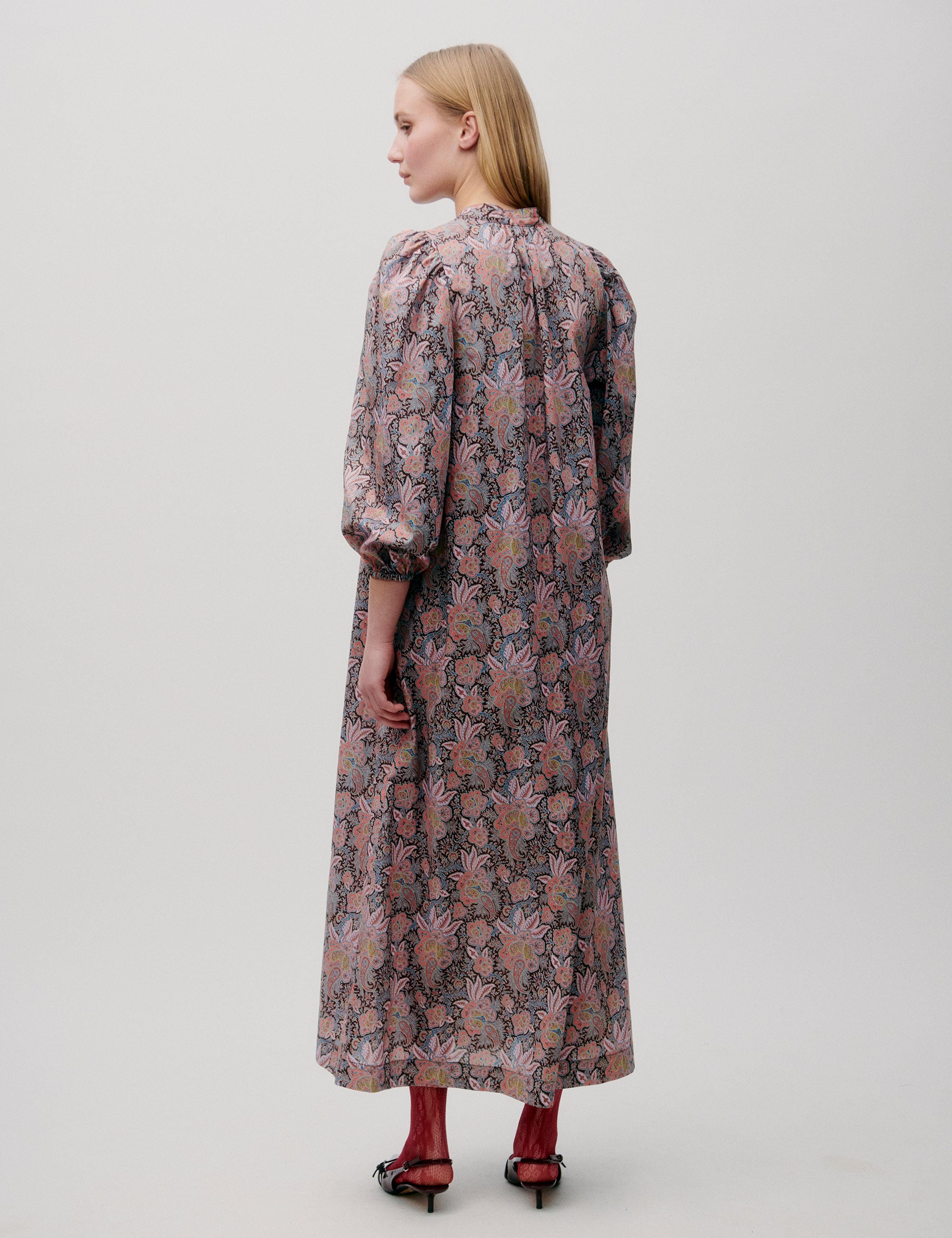 Woman wearing a long pink patterned dress with puff sleeves and gathered neckline