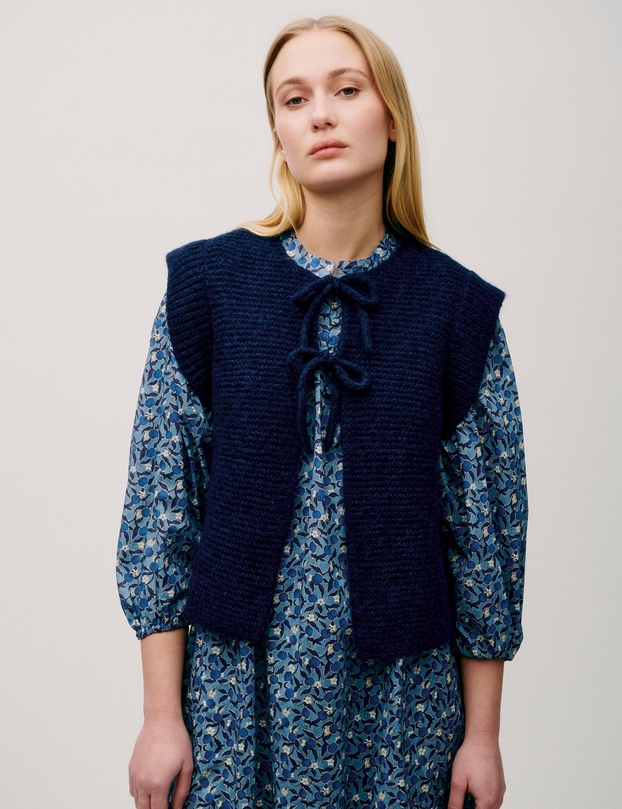 Woman in long sleeved dress with blue flower pattern and dark blue knitted wool vest