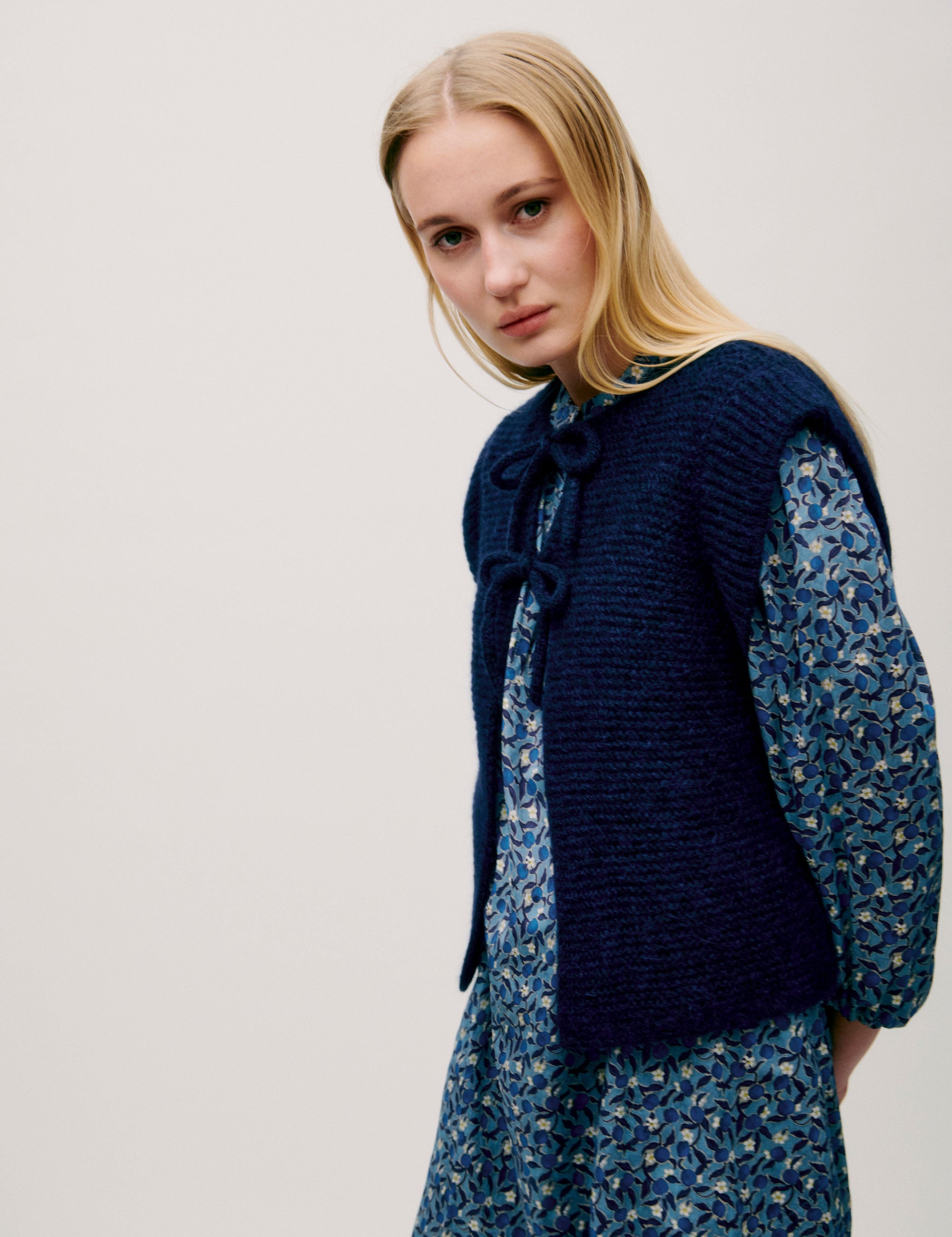 Woman in long sleeved dress with blue flower pattern and dark blue knitted wool vest