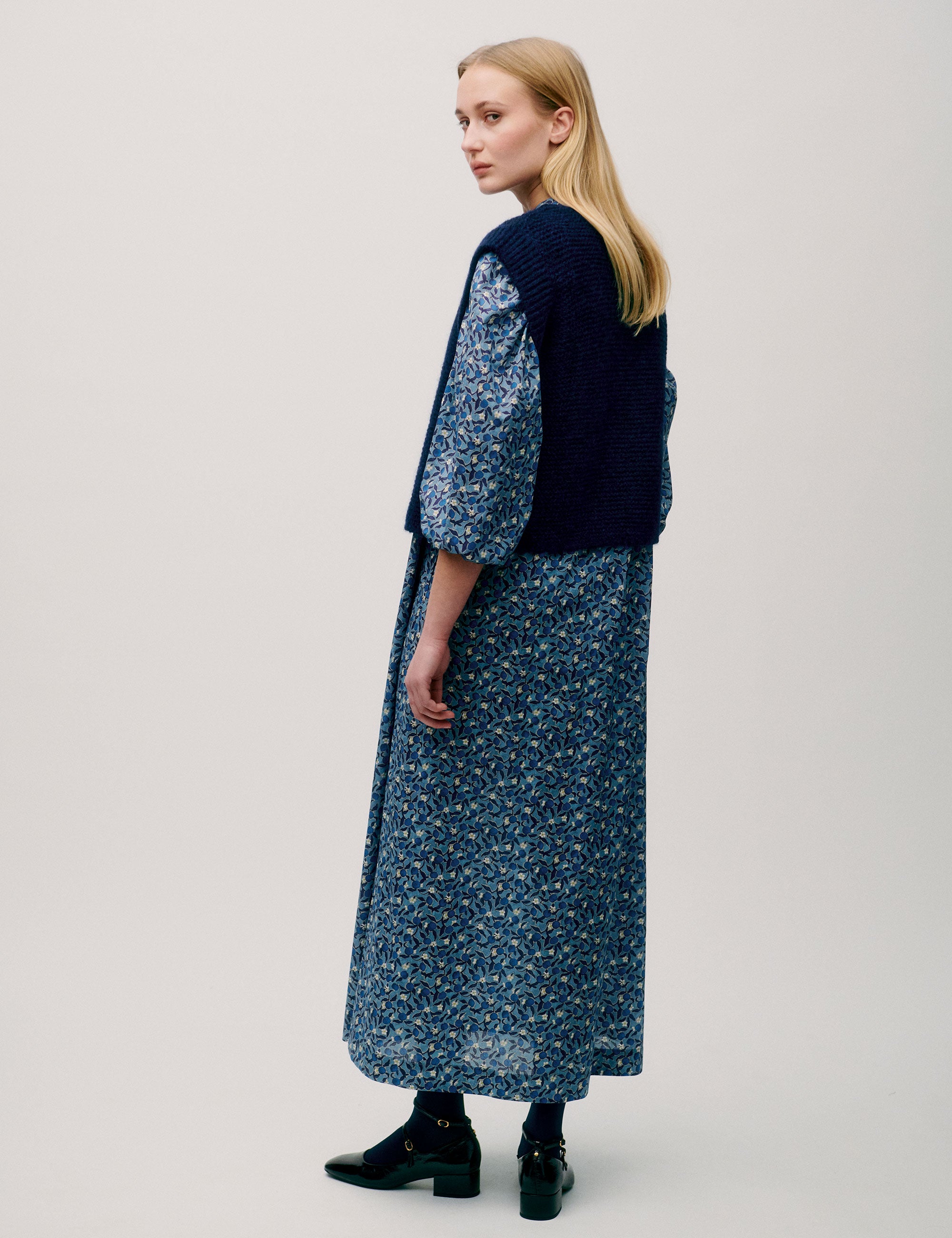 Woman in long sleeved maxi dress with blue flower pattern and dark blue knitted wool vest