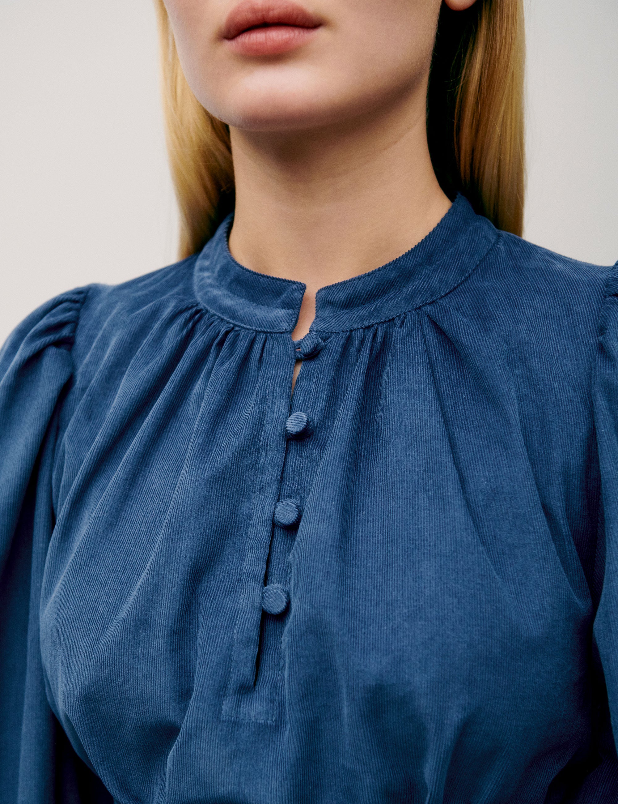 Close-up of pleated neckline and fabric-covered buttons on blue corduroy dress