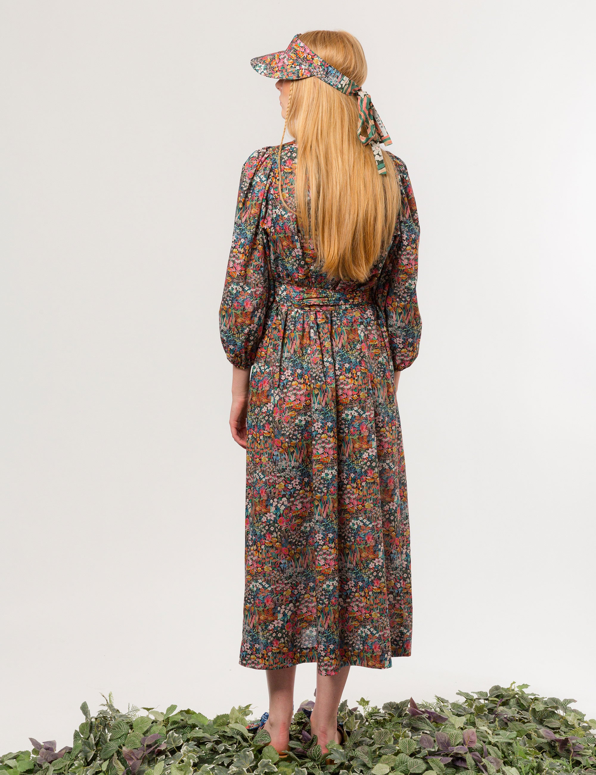 Woman in multicolored floral patterned dress with long sleeves and sun shade cap with multicolored flower pattern