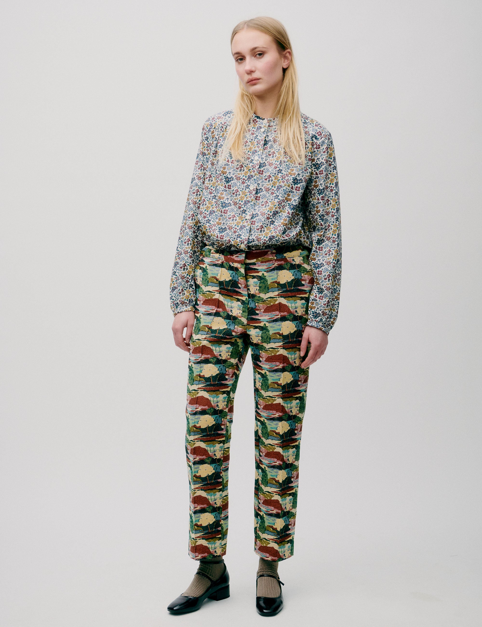 Woman wearing slim-fit trousers with abstract multicolor print, paired with a floral blouse