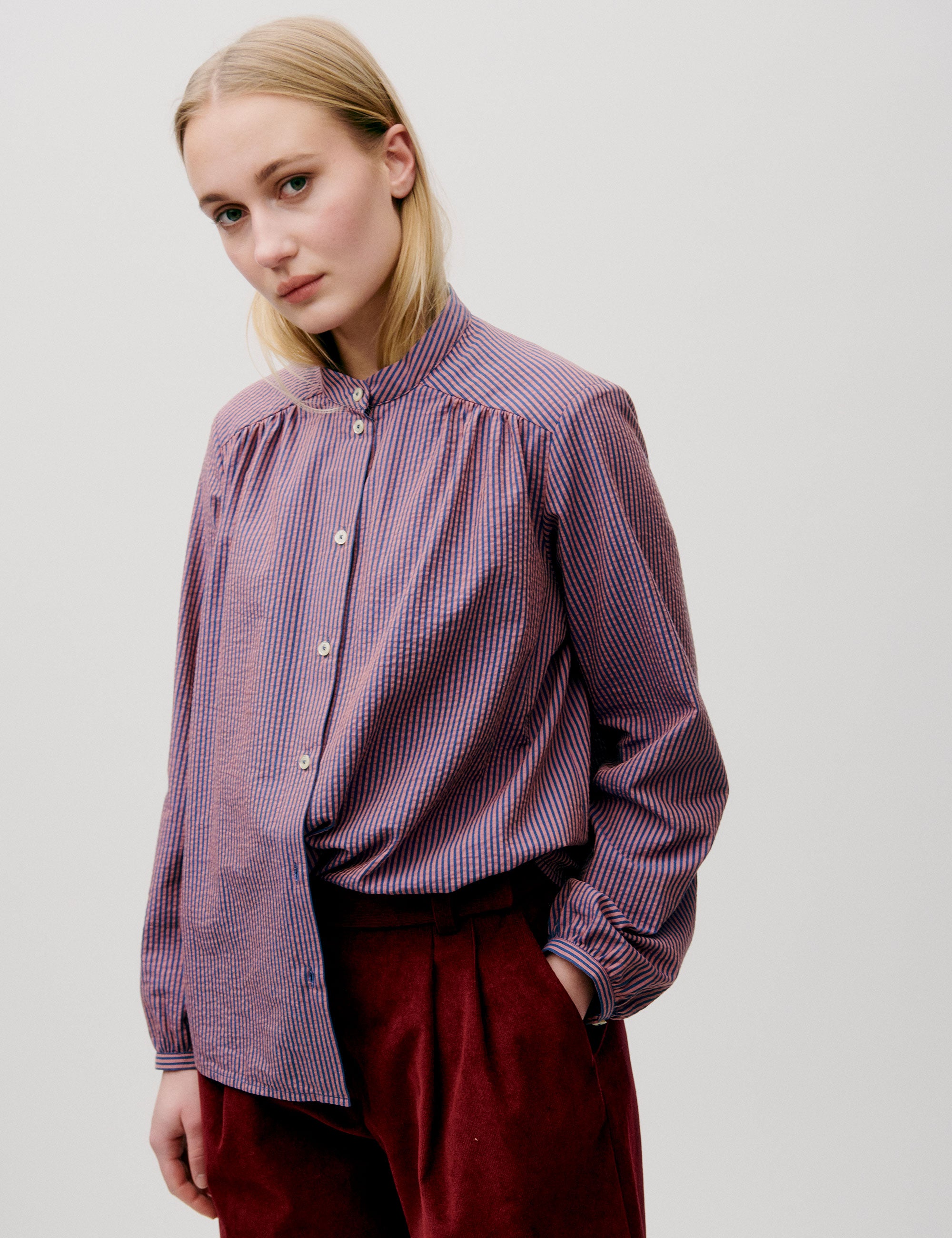 Woman in long sleeved pink striped shirt and red trousers