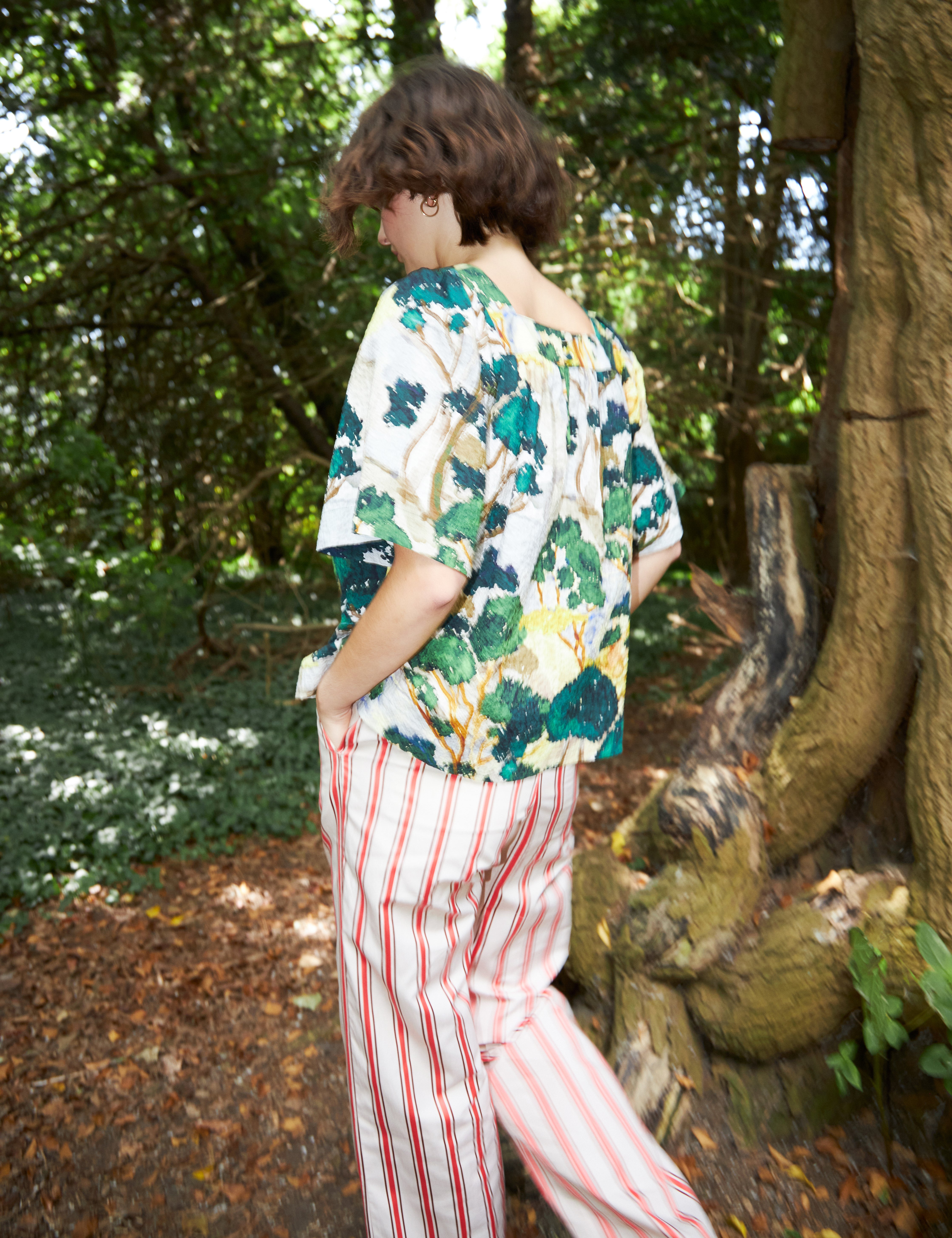 Woman in red and white striped pants and loose fit blouse with short sleeves in green yellow and white artistic patterned cotton