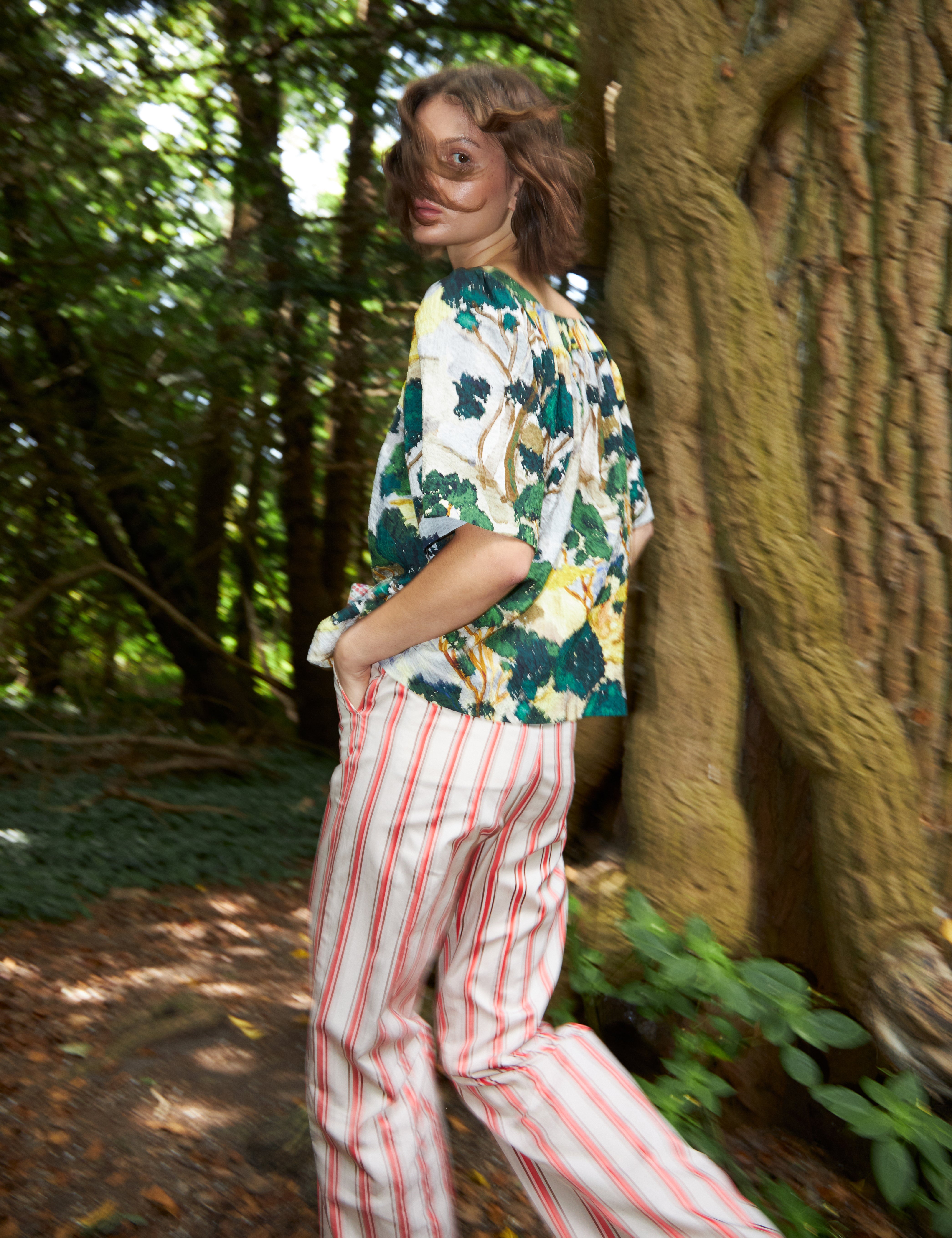 Woman in red and white striped pants and loose fit blouse with short sleeves in green yellow and white artistic patterned cotton