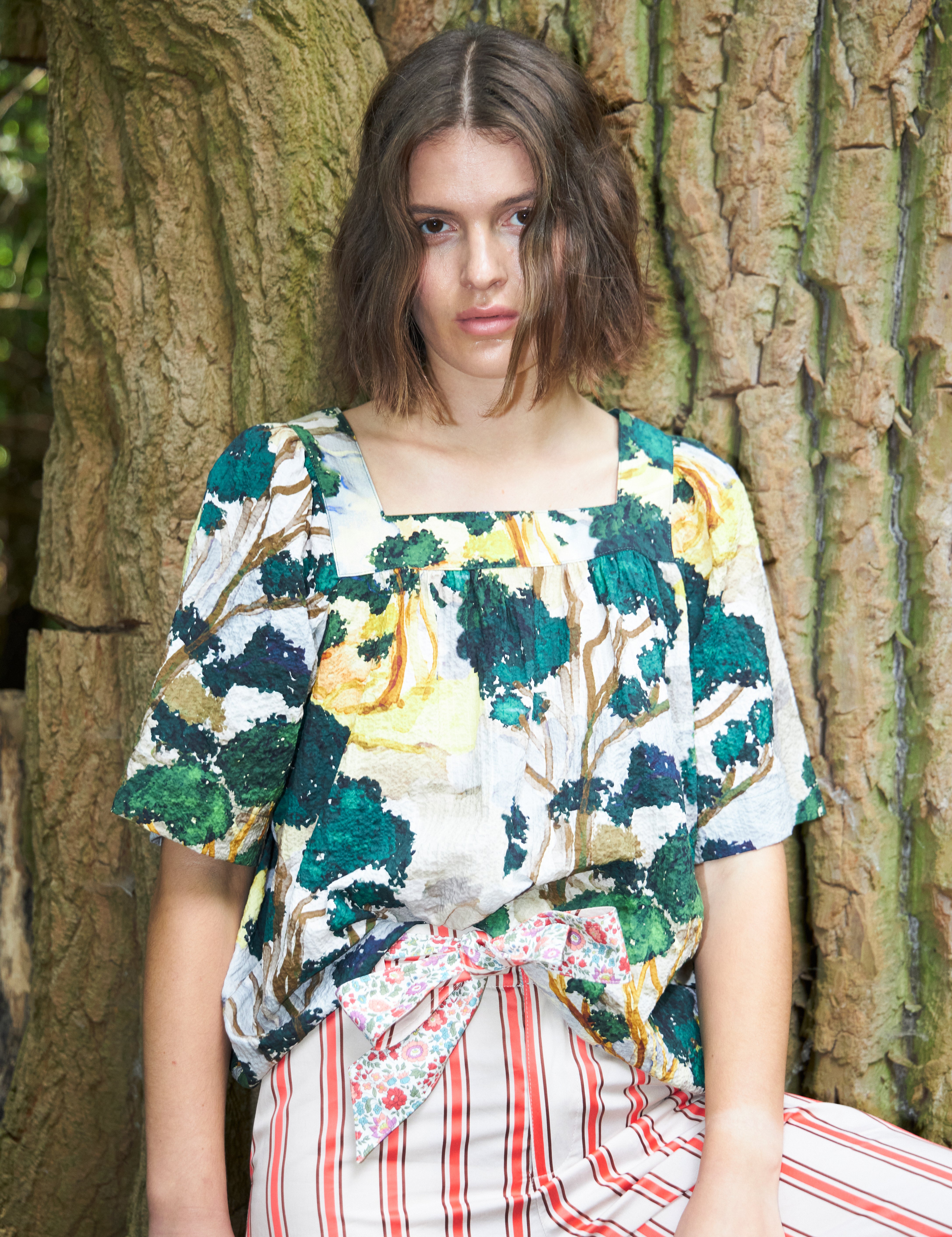 Woman in red and white striped pants with floral print cotton belt and short sleeved blouse with artistic print in green white and yellow