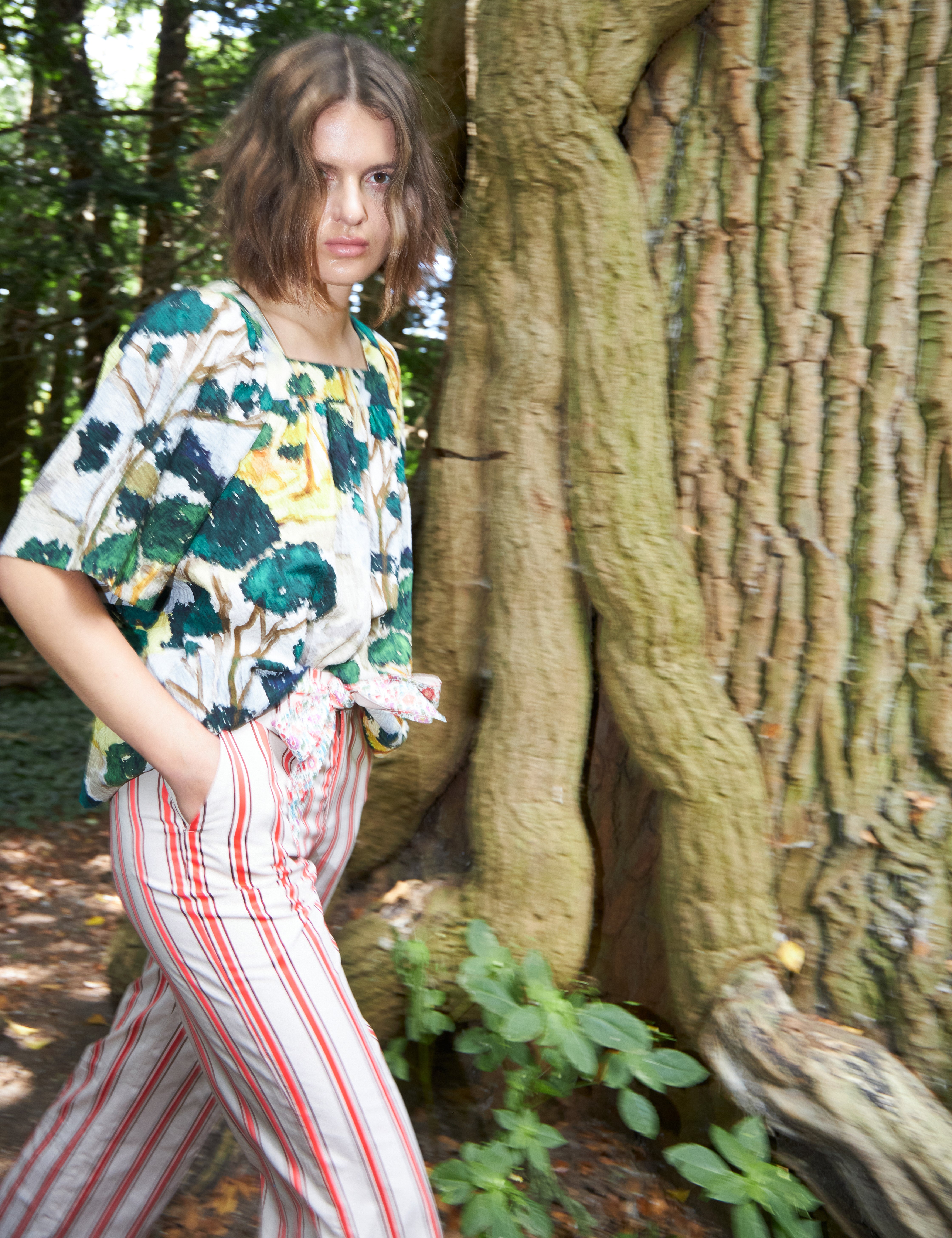 Woman in red and white striped pants and loose fit blouse with short sleeves in green yellow and white artistic patterned cotton