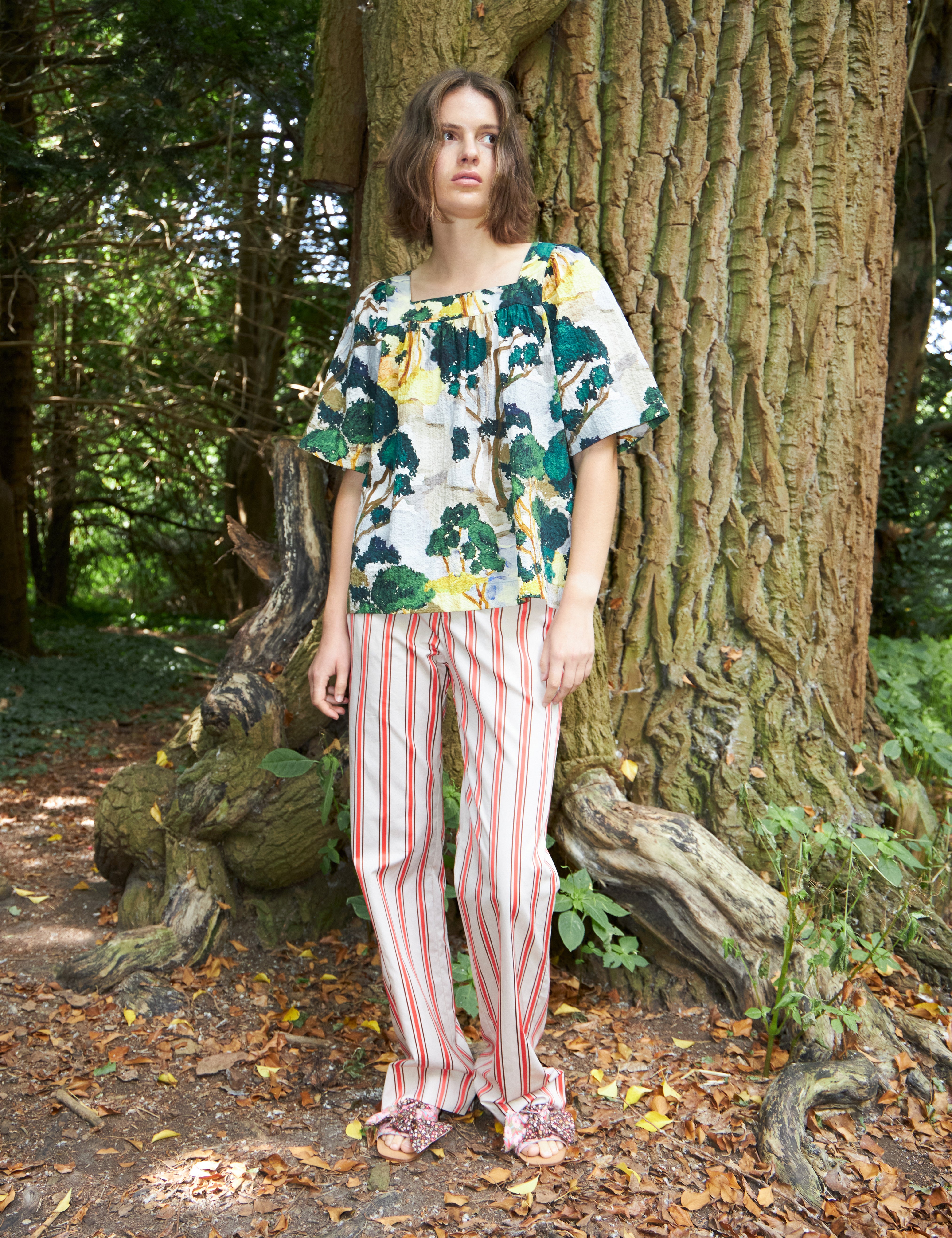 Woman in red and white striped pants and loose fit blouse with short sleeves in green yellow and white artistic patterned cotton