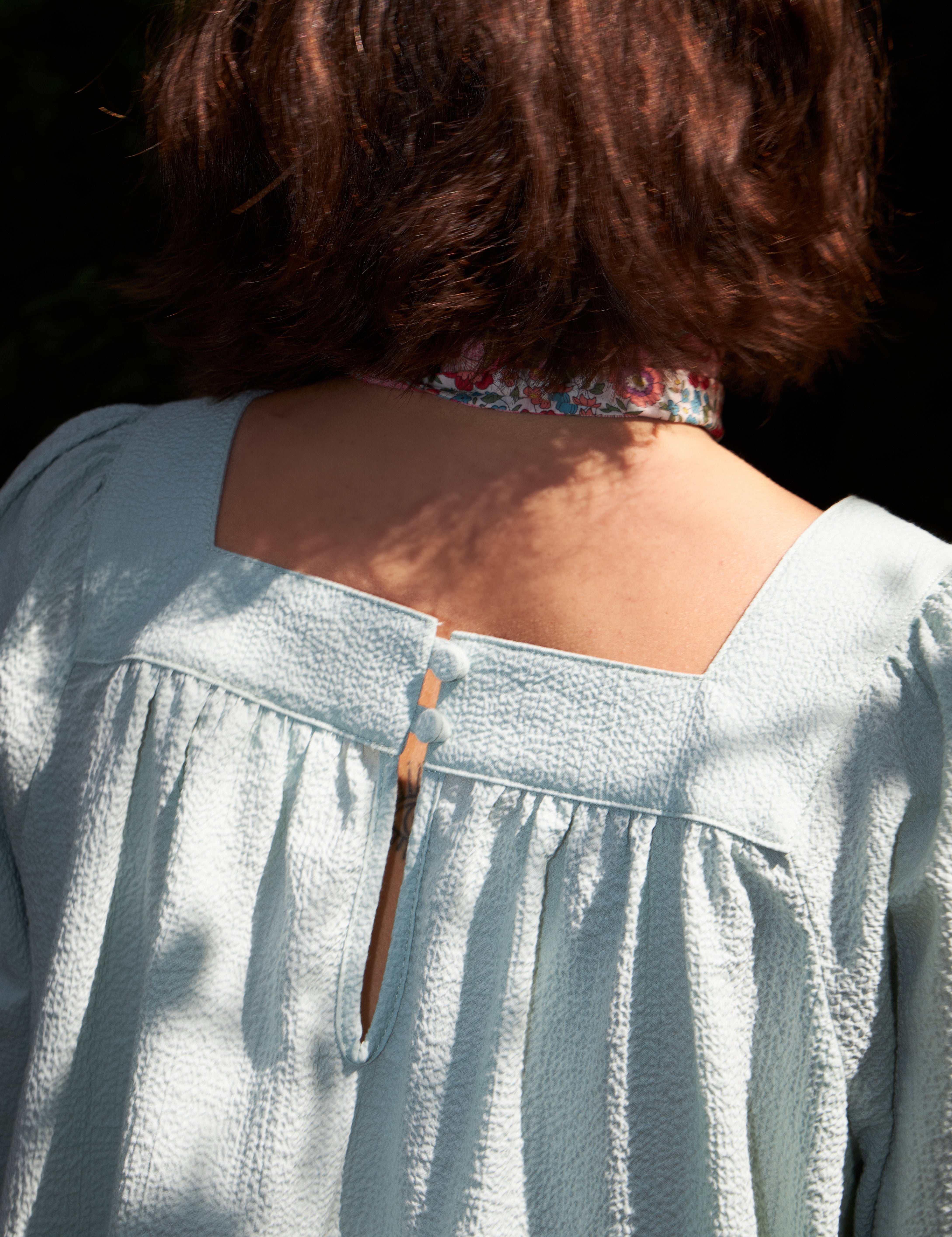 Woman in light blue loose fit seersucker blouse with short sleeves and bandana scarf around neck