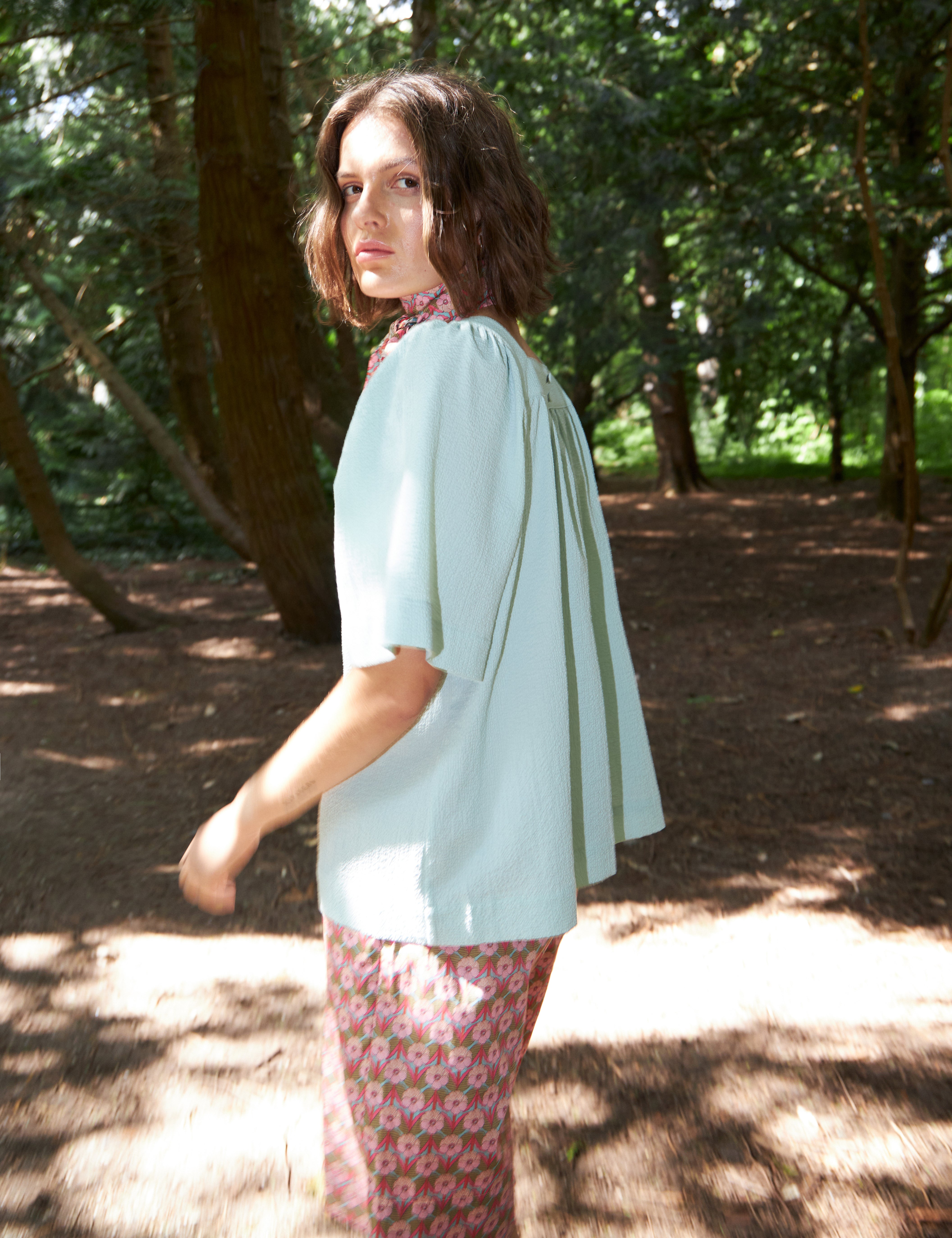 Woman in pink floral patterned shorts and light blue loose fit seersucker blouse with short sleeves and bandana scarf around neck