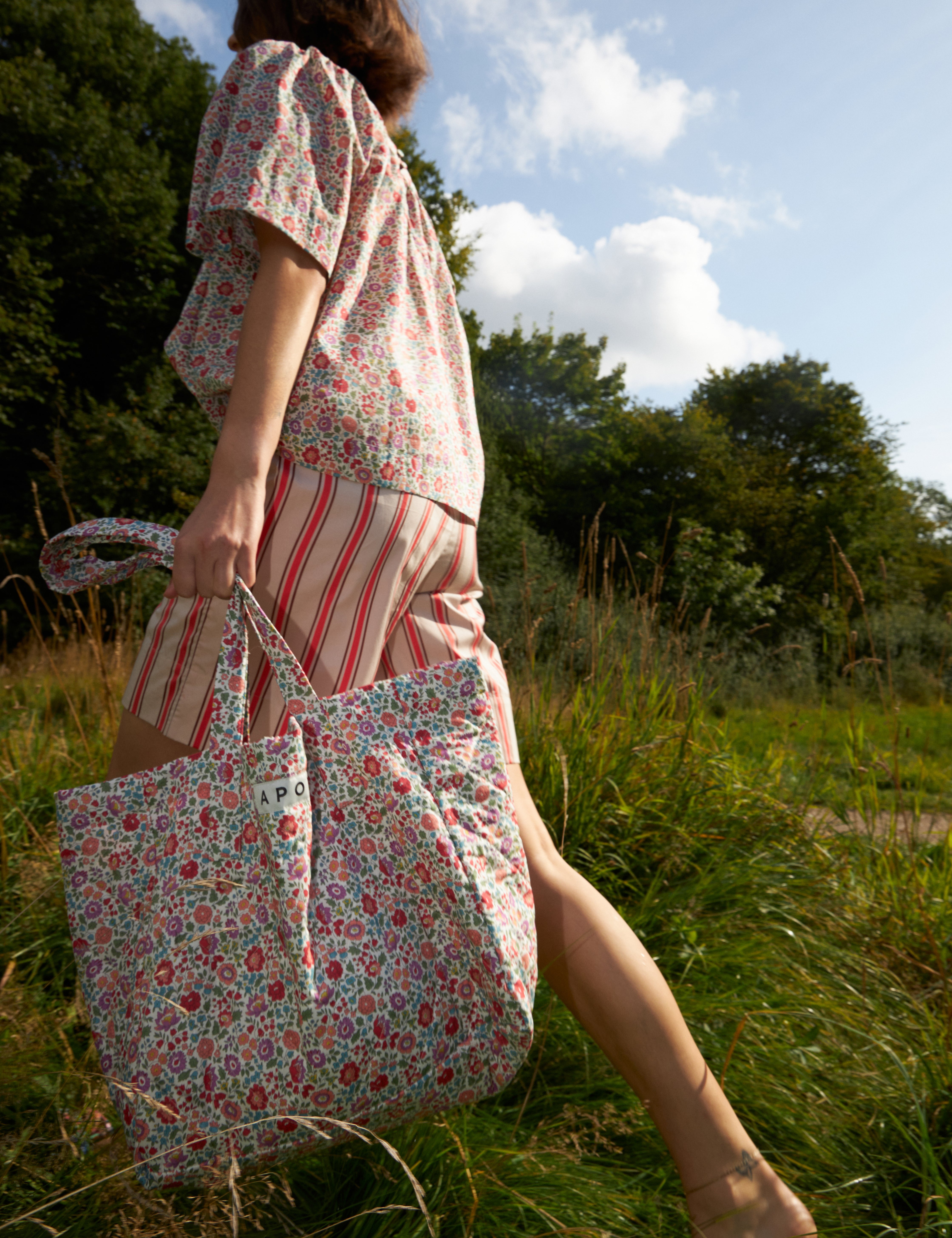 Woman in red and white striped shorts and multi-colored floral print shirt carrying a floral print tote bag