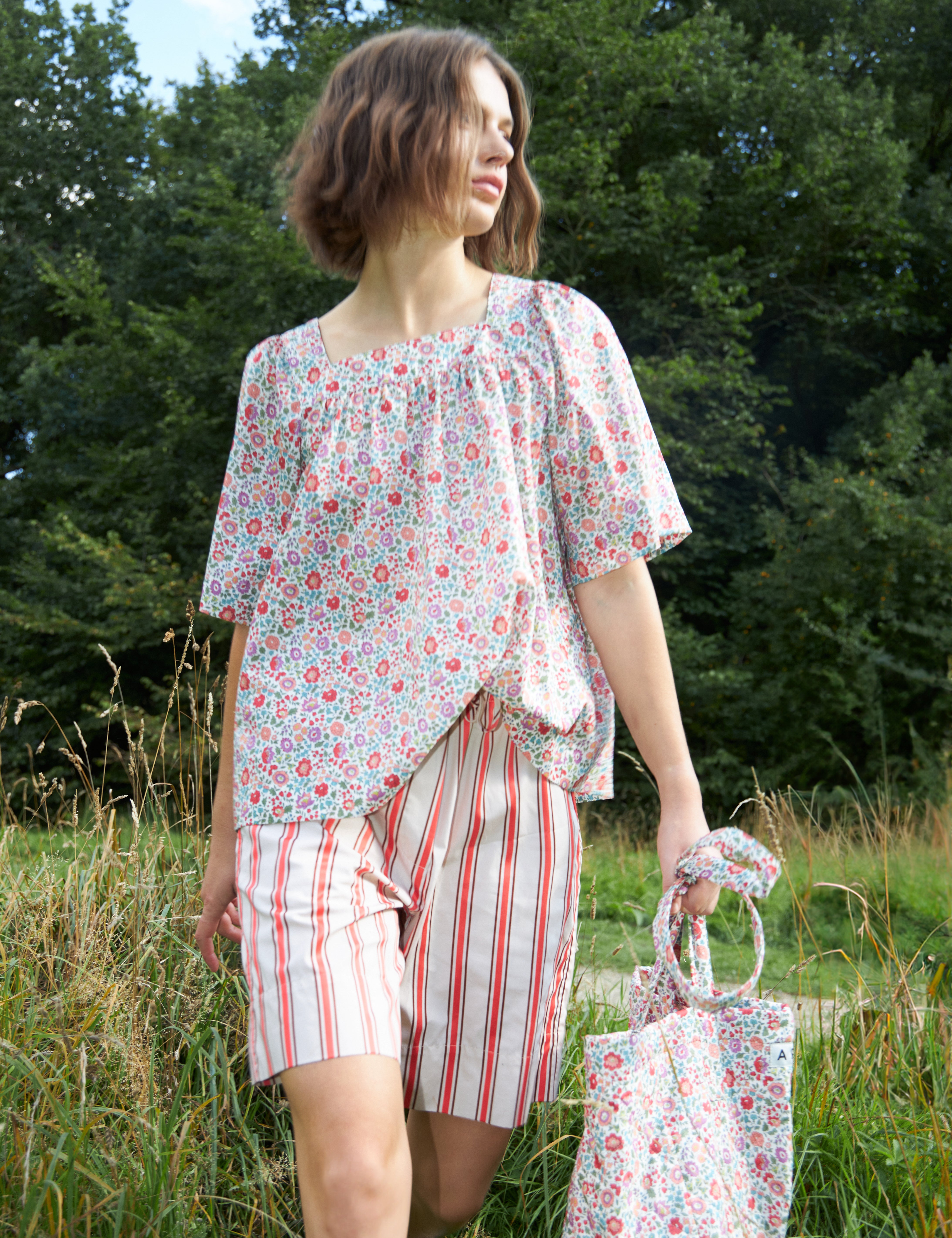 Woman in red and white striped shorts and loose fit blouse with short wide sleeves in multi-colored floral patterned Liberty cotton