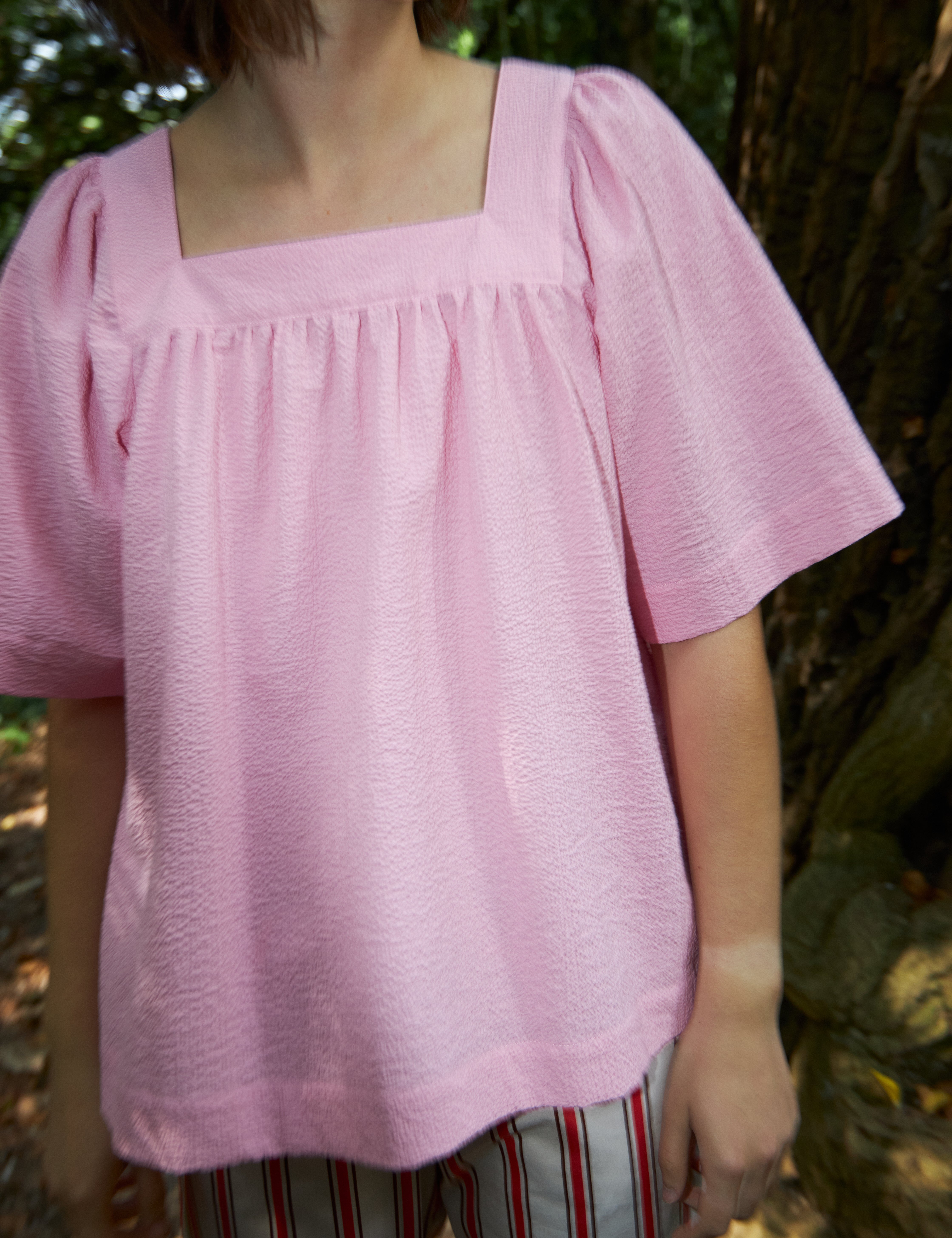 Woman in red and white striped pants and loose fit pink blouse with short wide sleeves