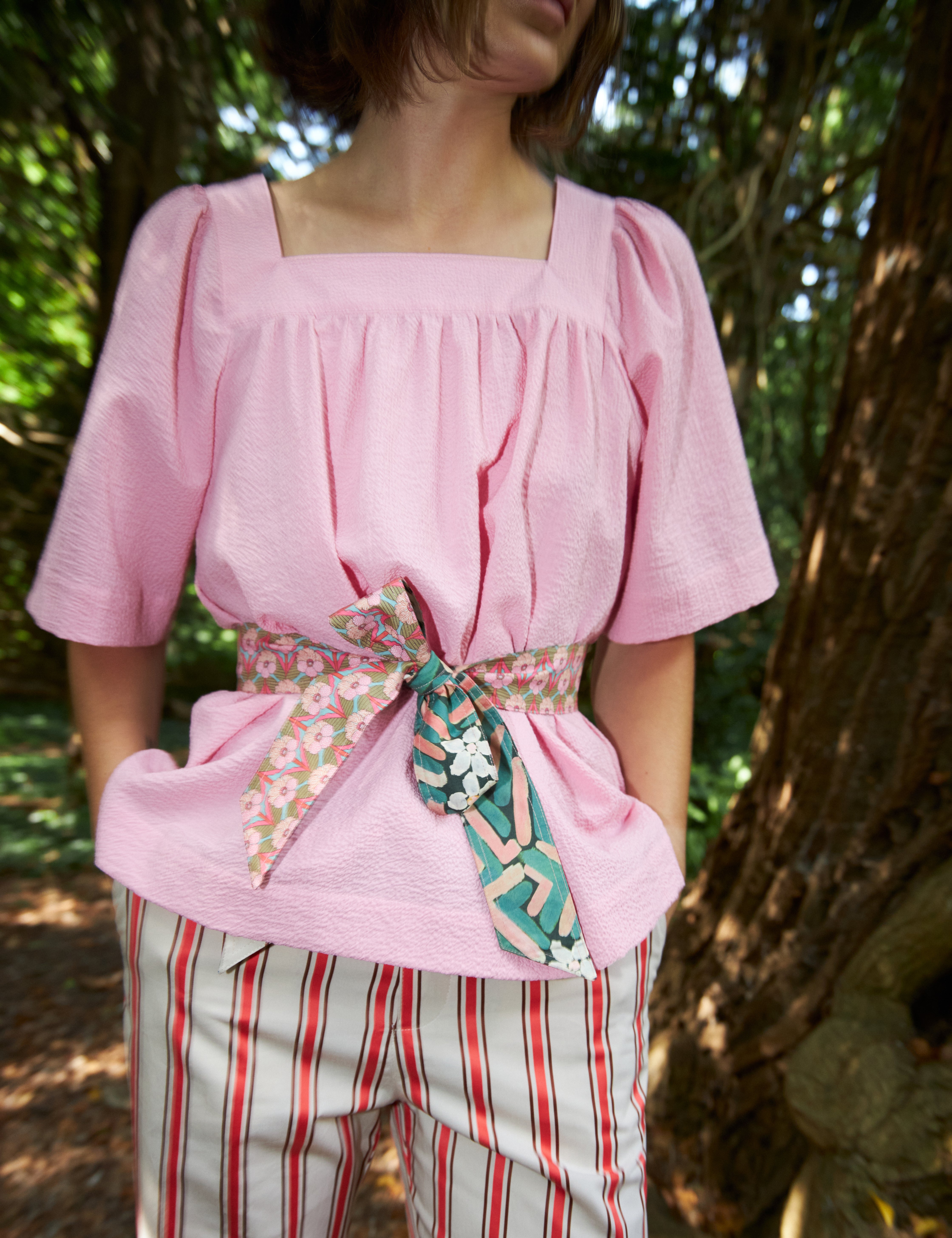 Woman in red and white striped pants and loose fit pink blouse with short wide sleeves and floral print cotton belt