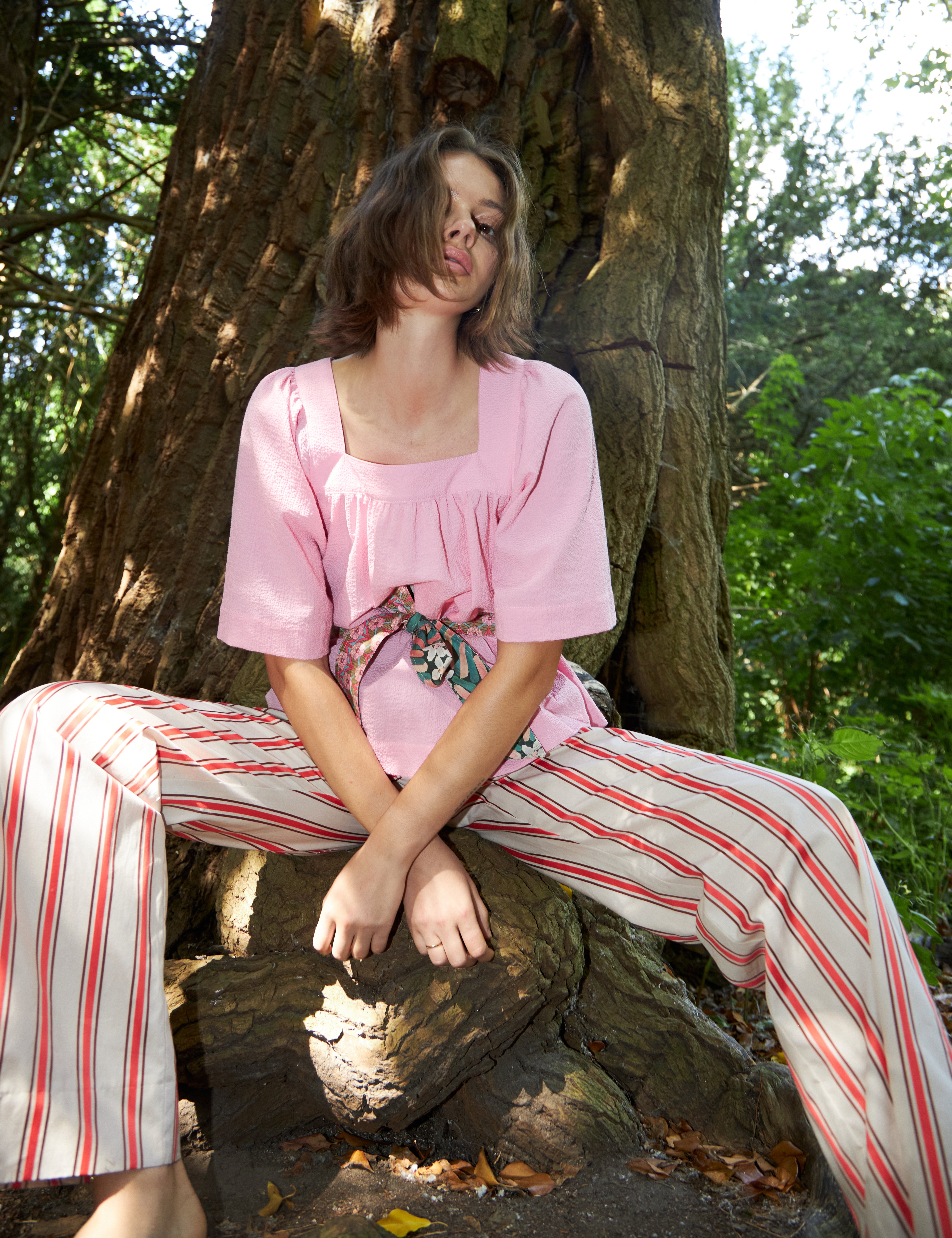 Woman in red and white striped pants and loose fit pink blouse with short wide sleeves and floral print cotton belt