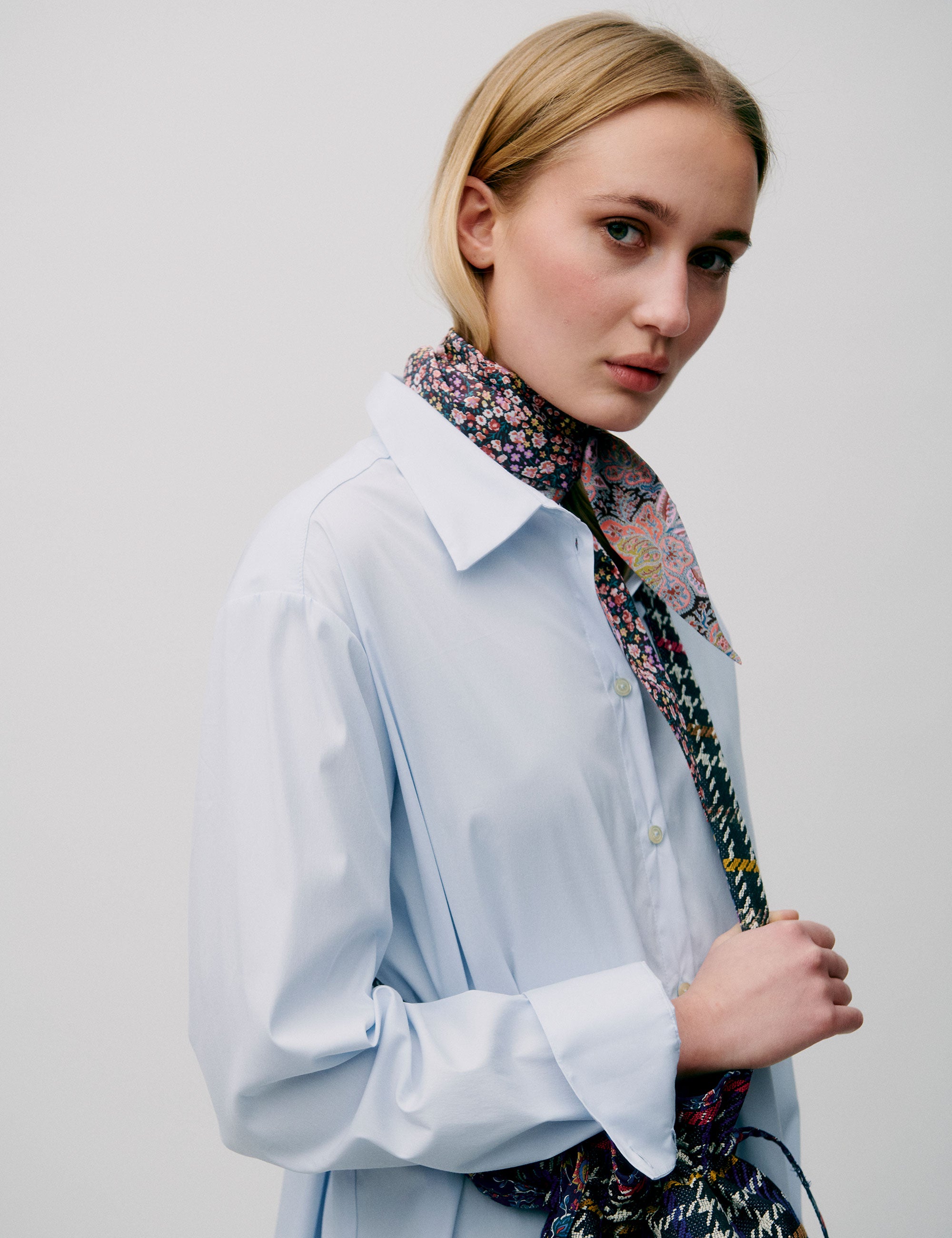 Woman in light blue straight cotton shirt with long sleeves carrying a check patterned crossbody bag