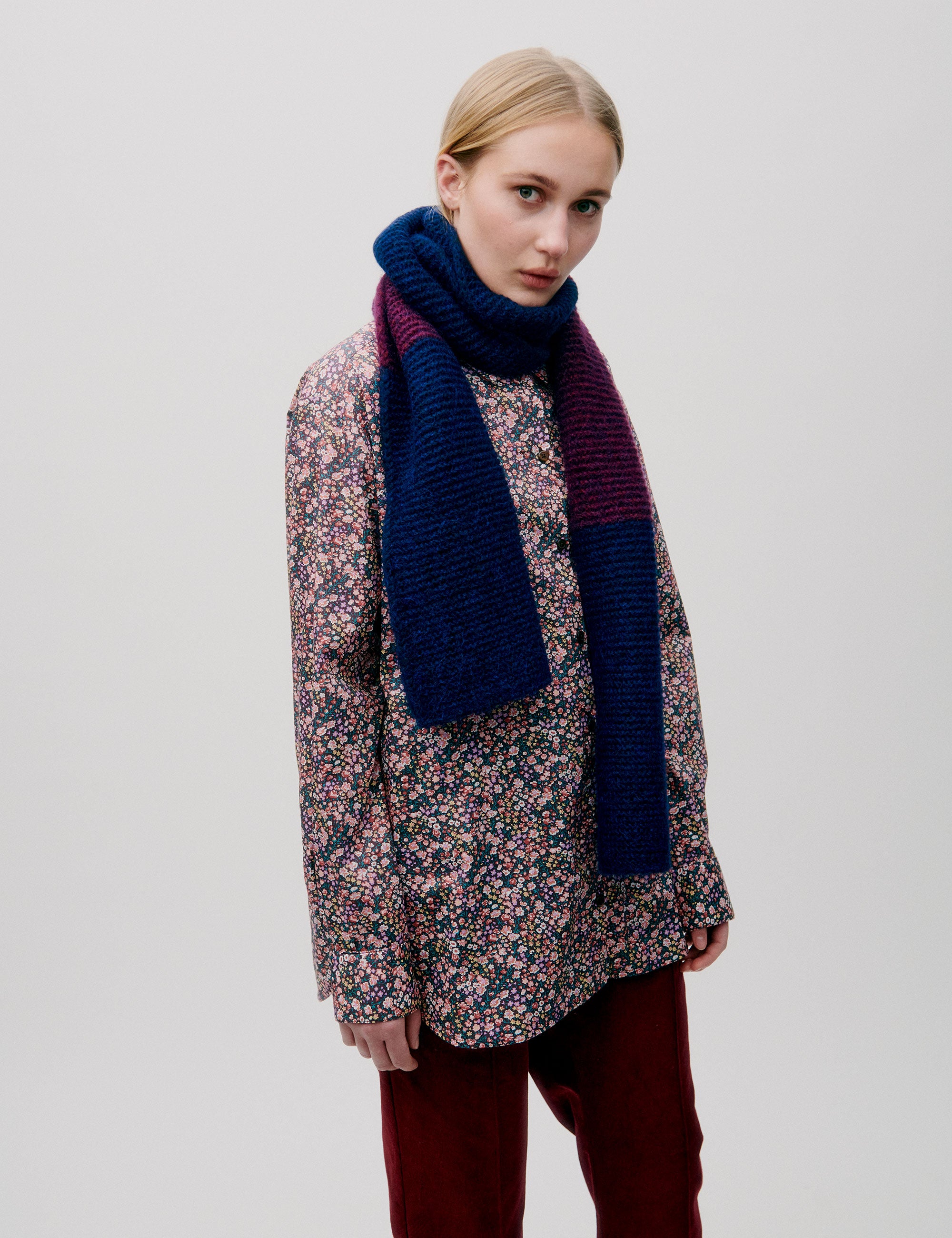 Woman wearing a multicolored floral blouse with a chunky color-block knit wool scarf in blue and burgundy