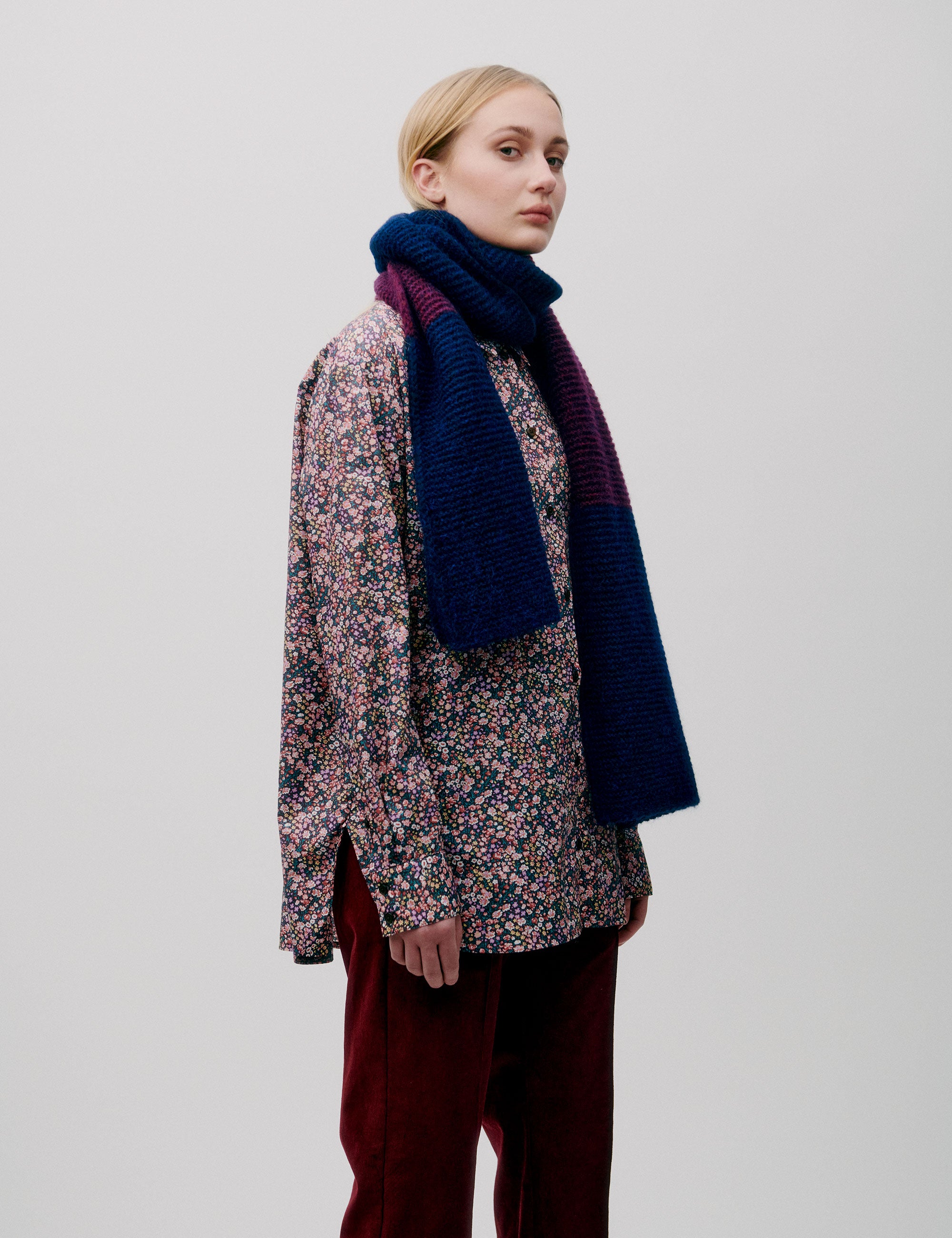 Woman wearing a multicolored floral blouse with a chunky color-block knit wool scarf in blue and burgundy
