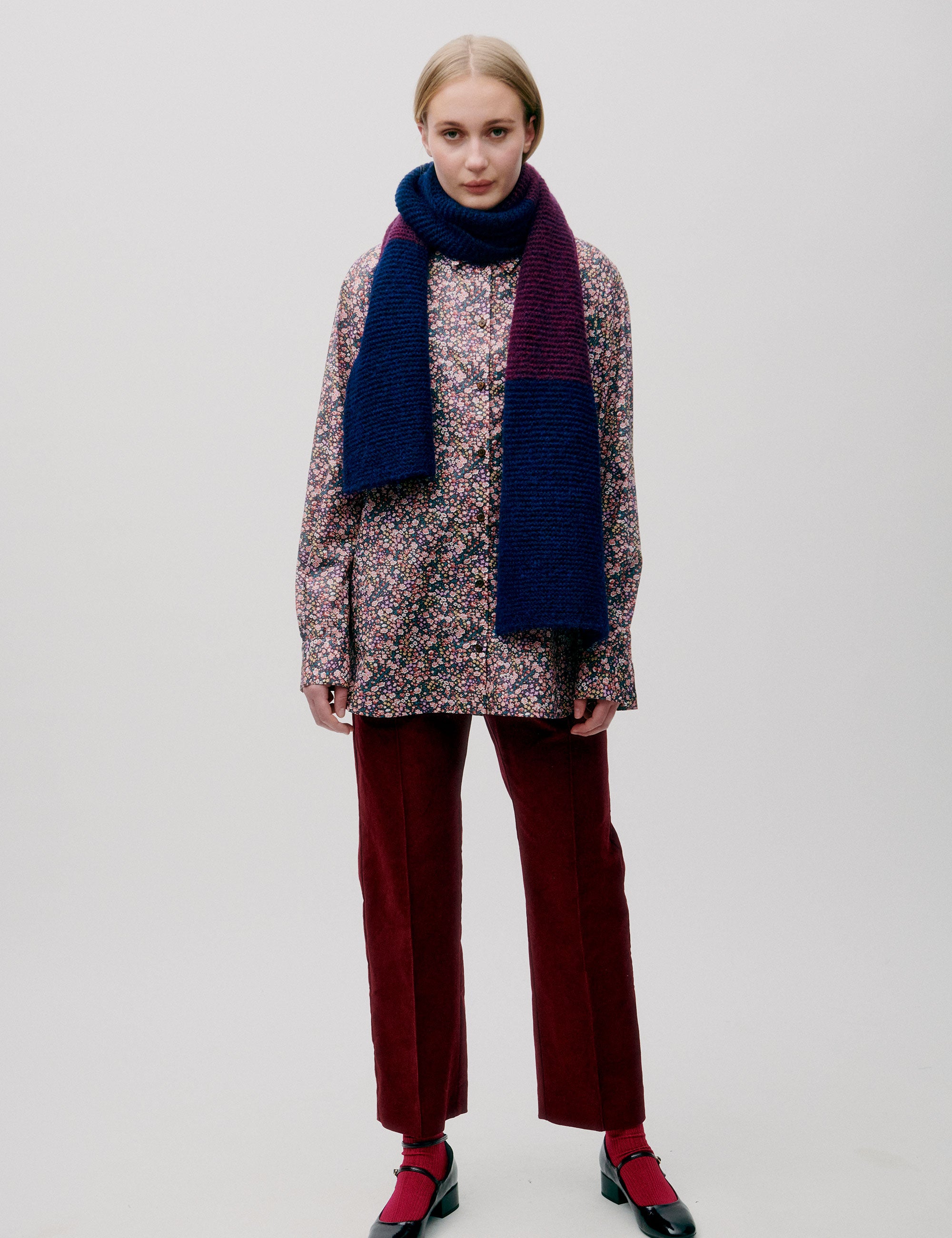 Woman wearing a multicolored floral blouse with a chunky color-block knit wool scarf in blue and burgundy