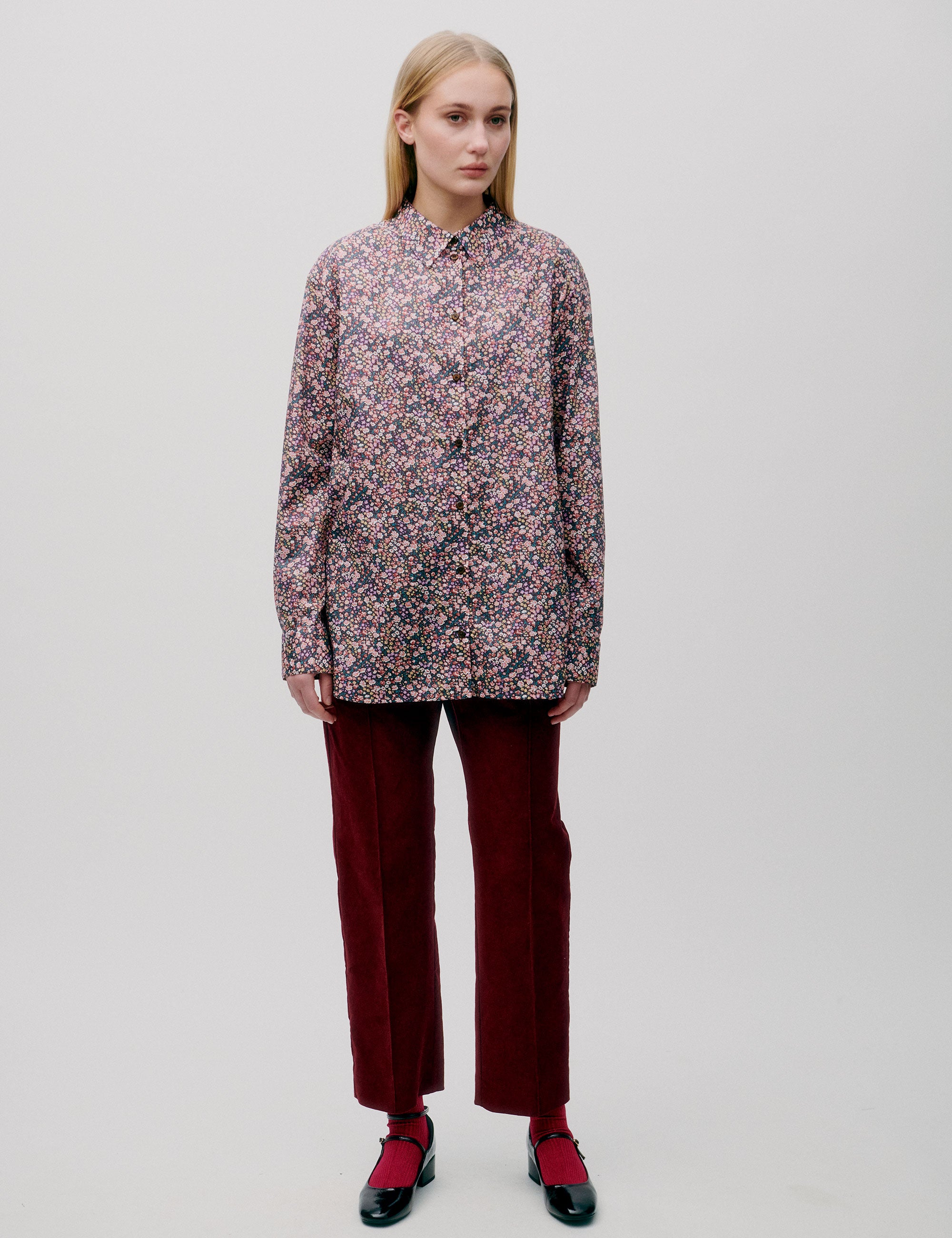 Woman in straight pink and blue small flower patterned shirt with long sleeves and dark red corduroy pants