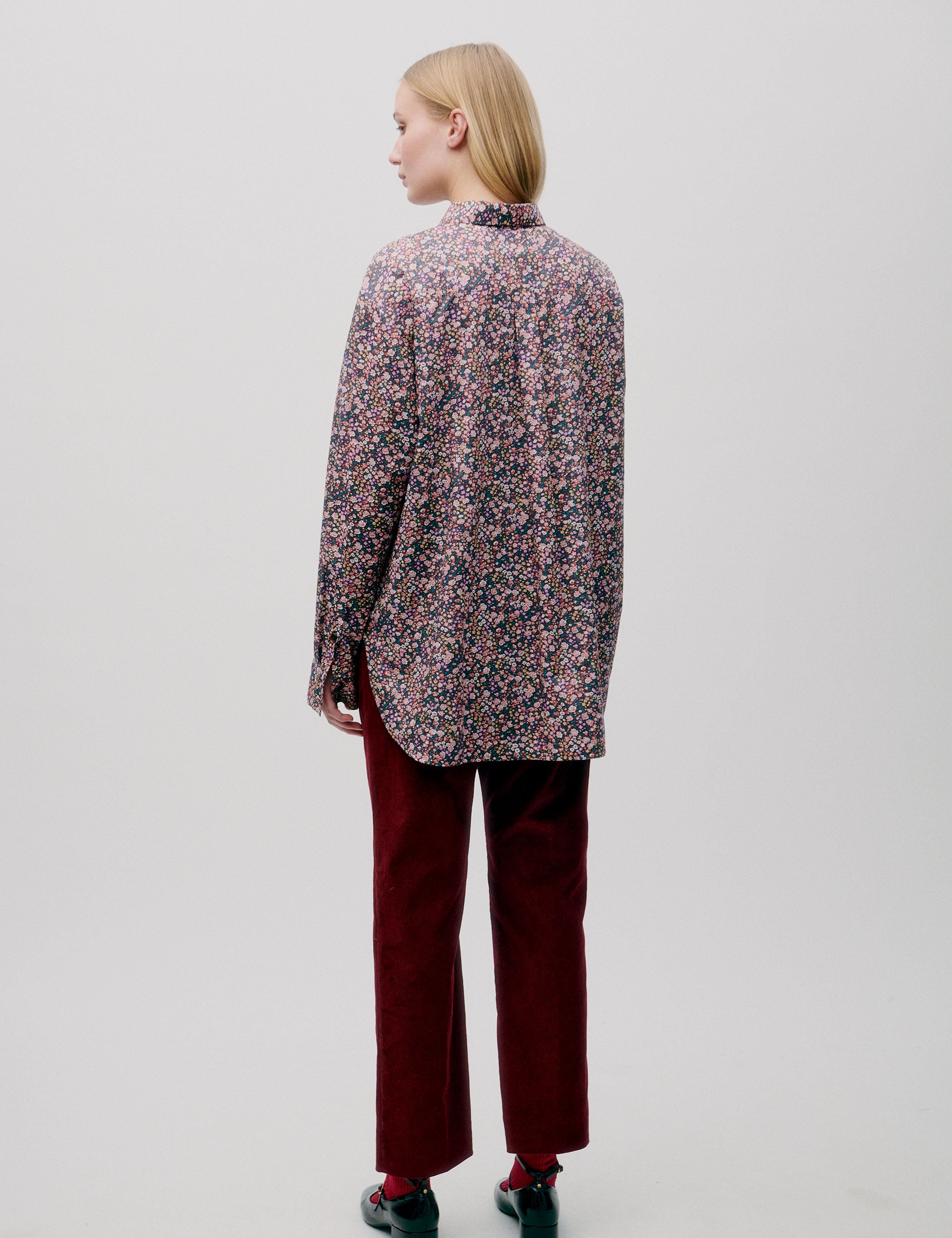 Woman in straight pink and blue small flower patterned shirt with long sleeves and dark red corduroy pants