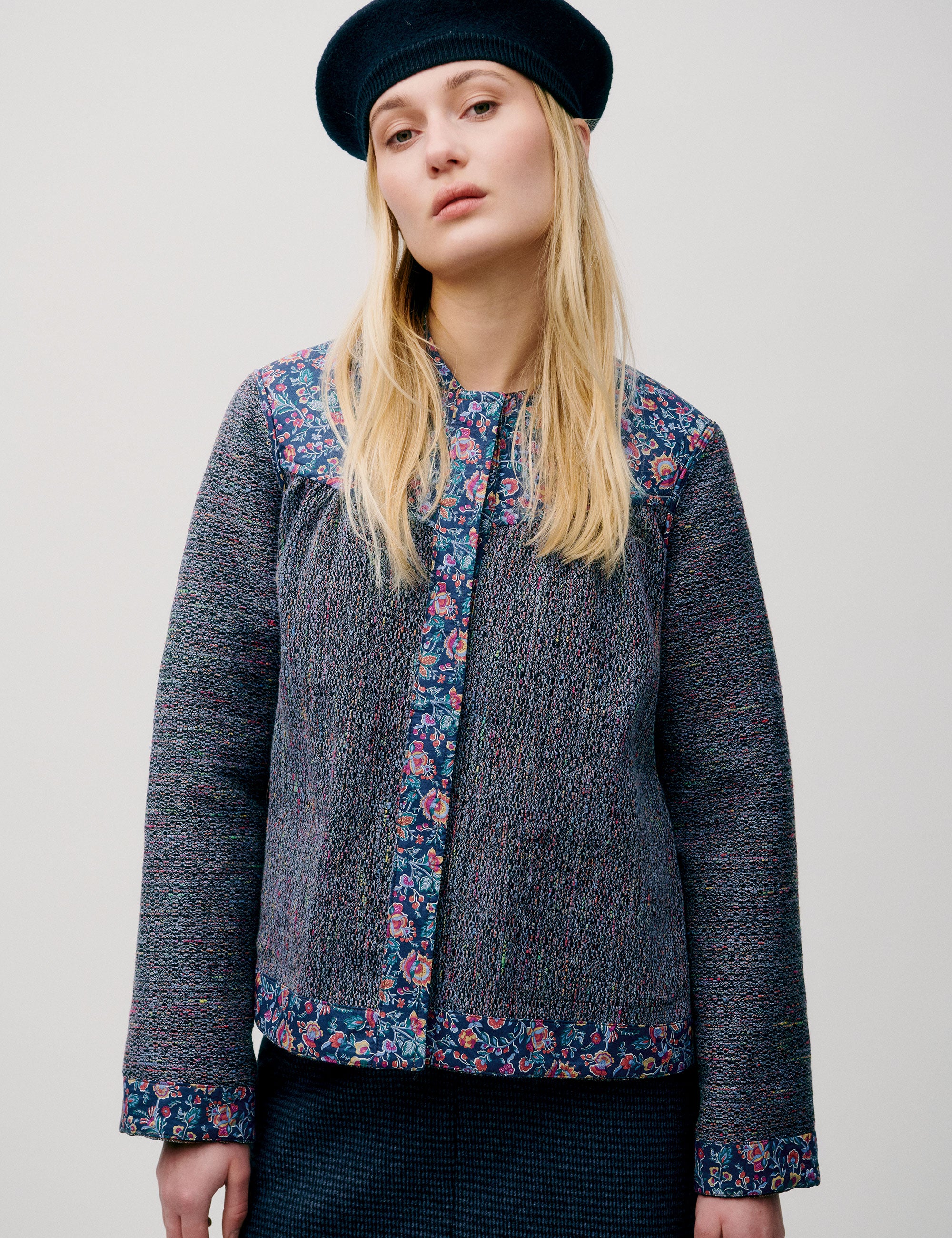 Woman in straight blue jacket with pink and blue floral details, wearing a beret and blue skirt