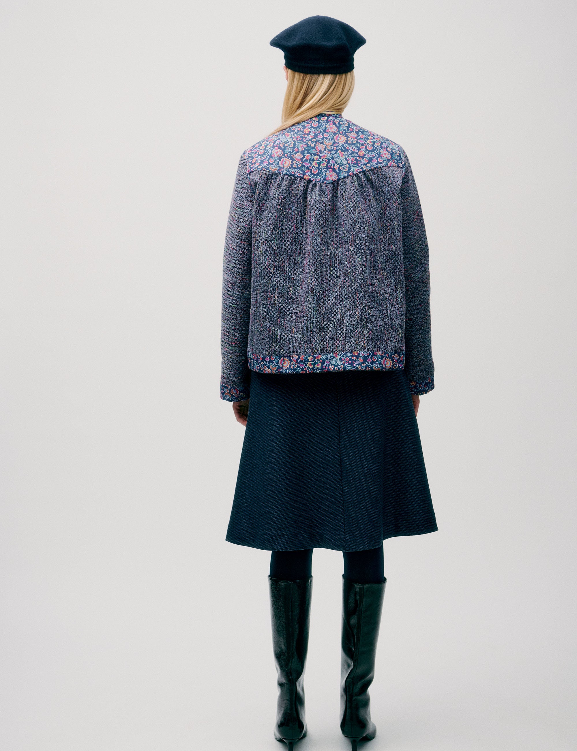Woman in straight blue jacket with pink and blue floral details, wearing a beret and blue skirt