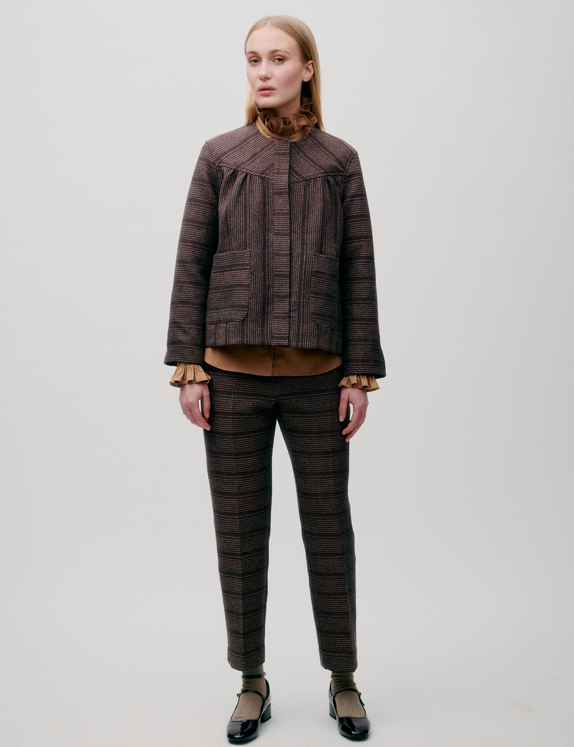 Woman wearing a brown wool jacket and matching patterned trousers, facing forward