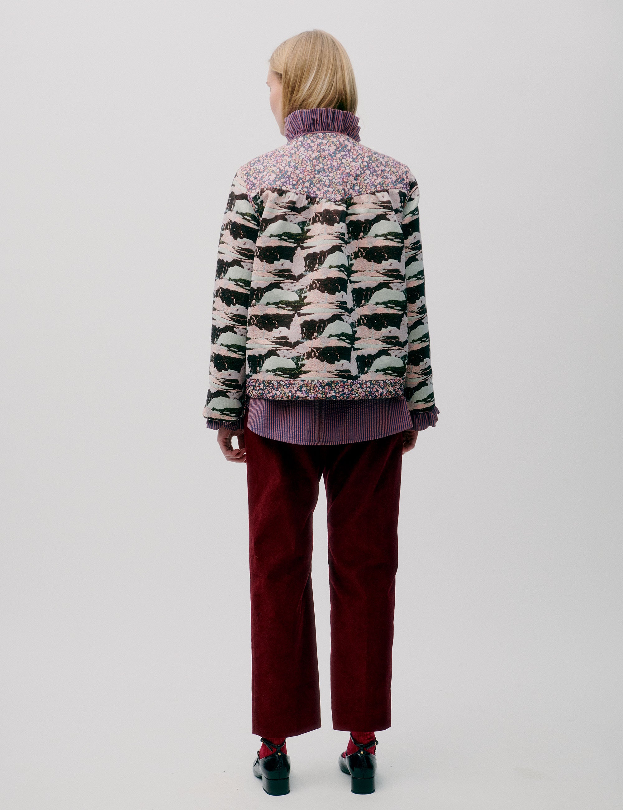 Woman in burgundy colored pants, pink striped shirt with frills and quilted jacket with floral and artistic print
