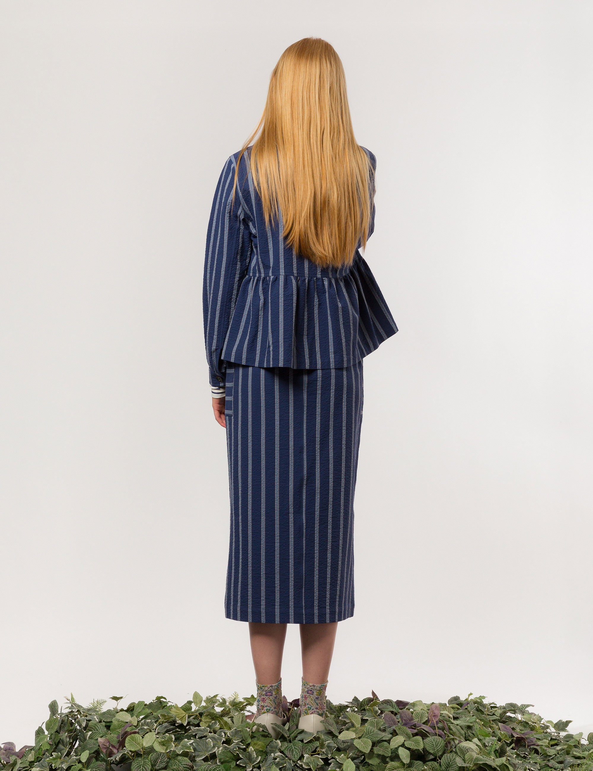 Woman in white and blue striped long sleeved women's jacket with buttons and round neck and matching skirt with pockets