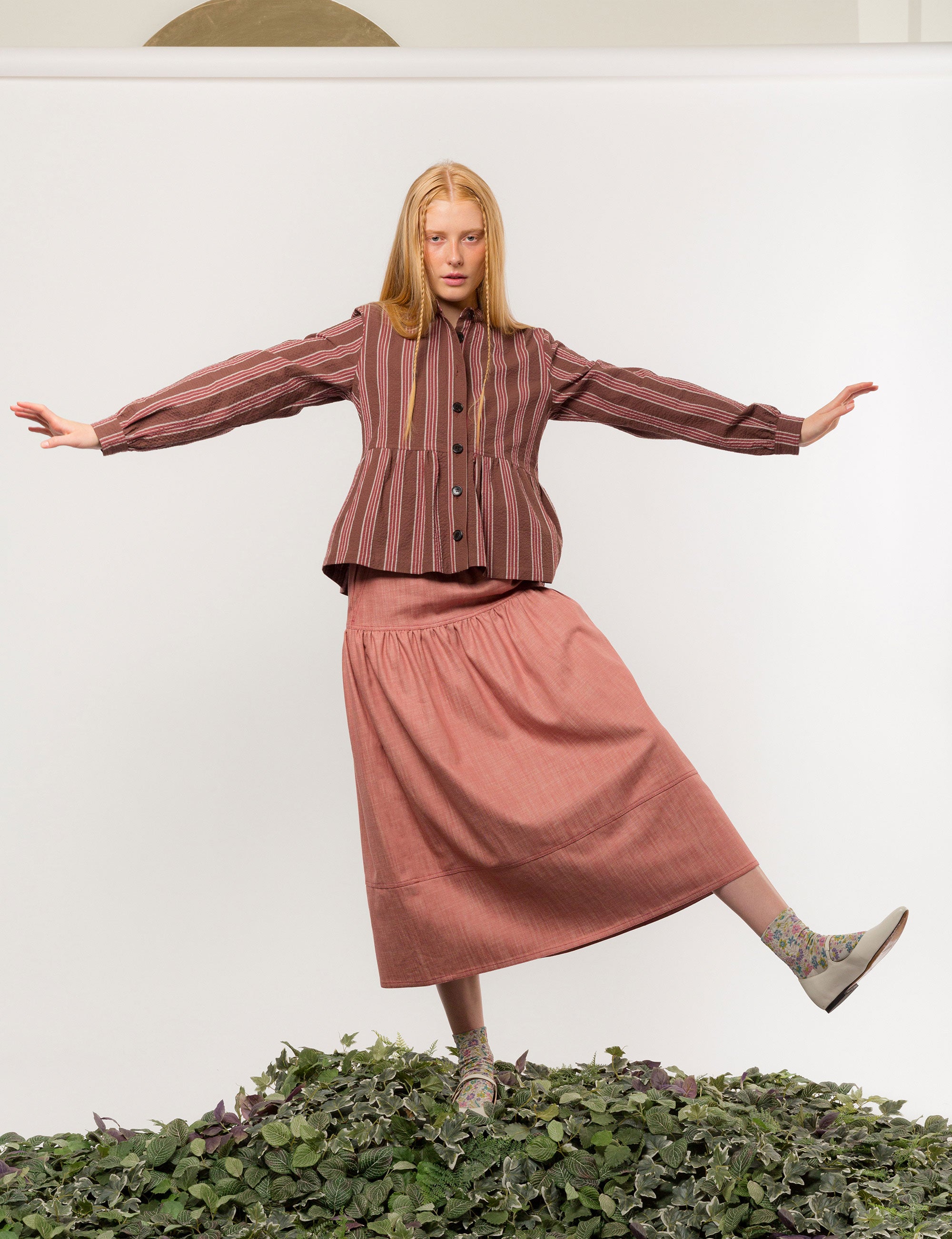 Woman in brown, white and red striped long sleeved cotton jacket with buttons and round neck and a pink long skirt