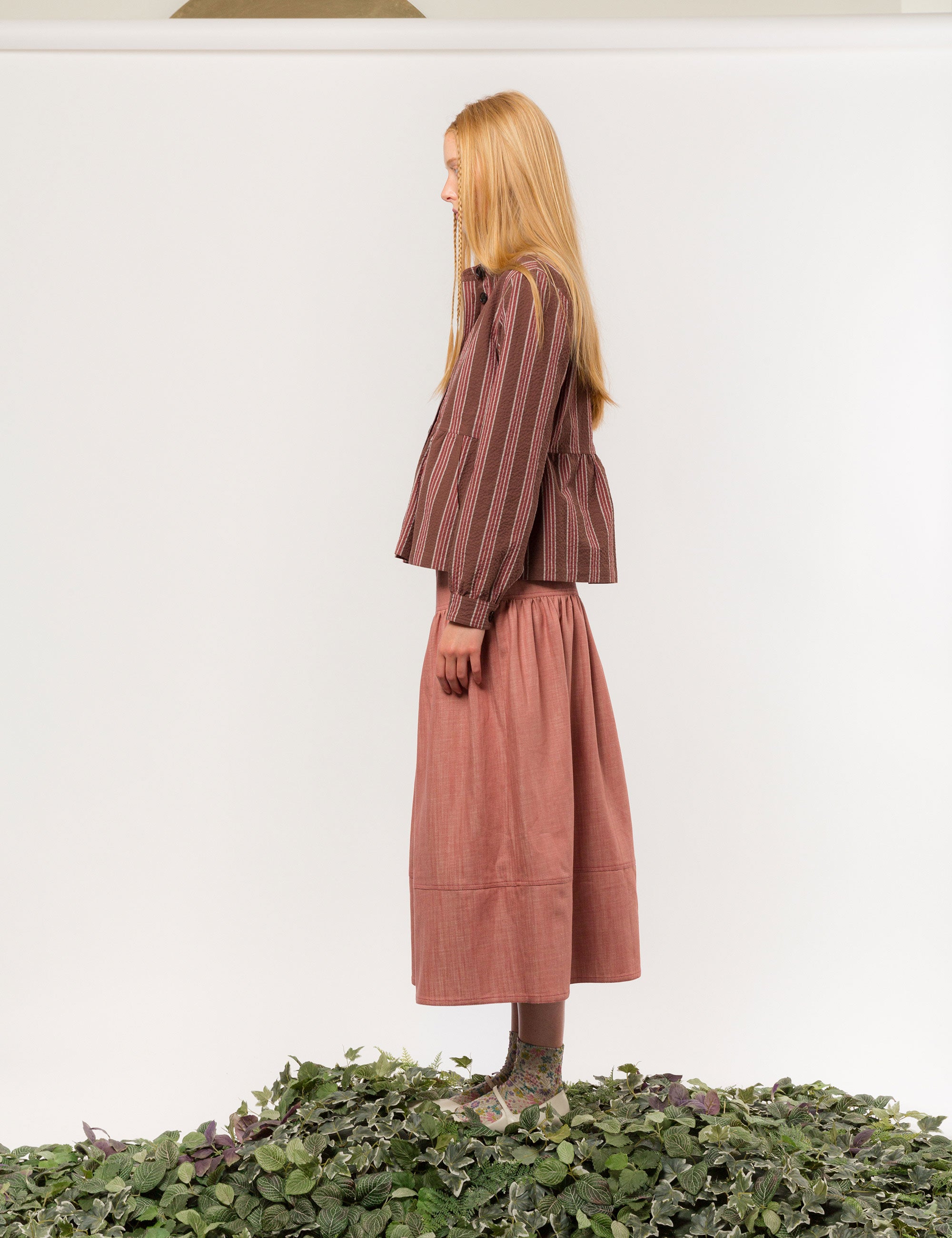 Woman in brown, white and red striped long sleeved cotton jacket with buttons and round neck and a pink long skirt