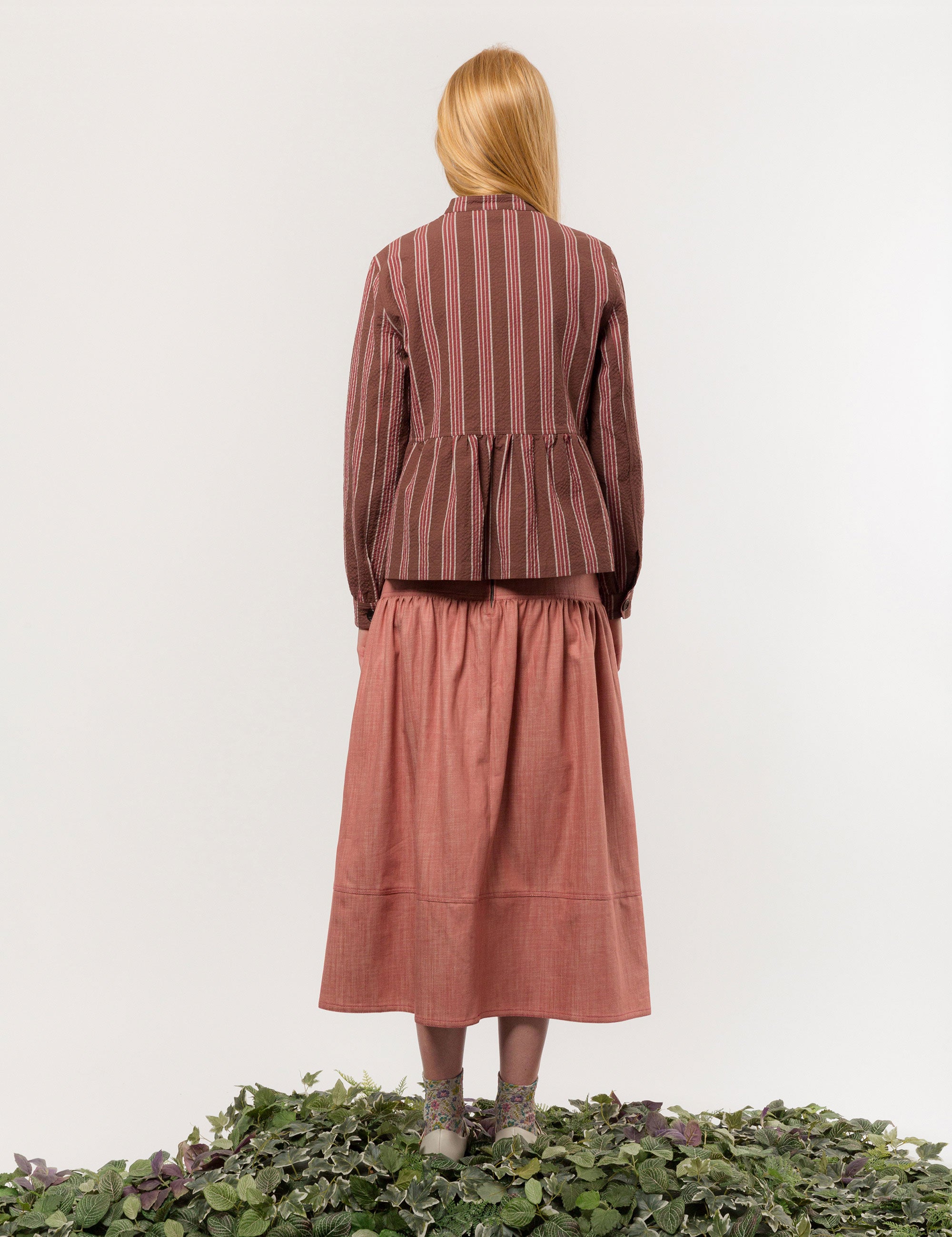 Woman in brown, white and red striped long sleeved cotton jacket with buttons and round neck and a pink long skirt