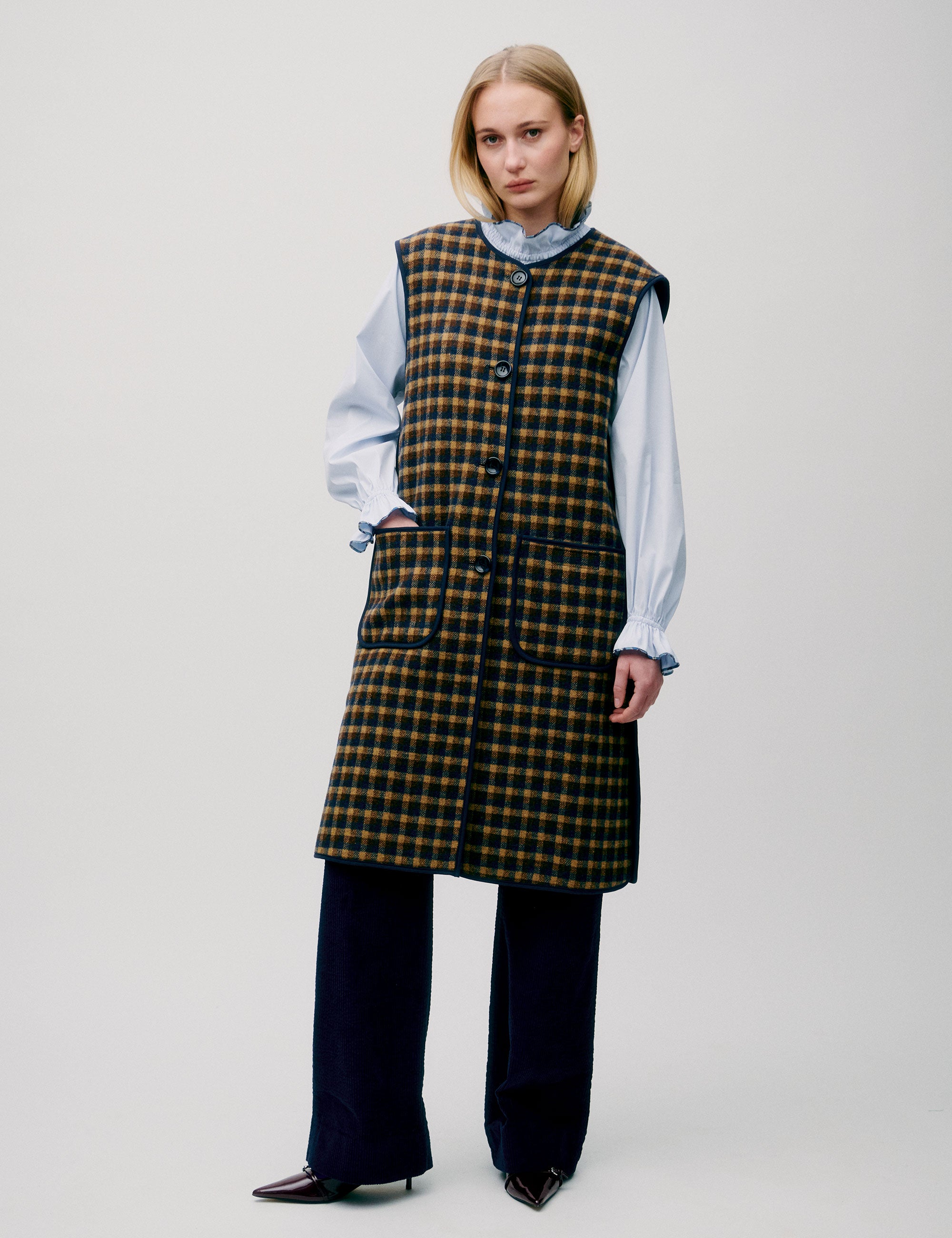 Woman in light blue shirt and long check patterned vest in yellow and black