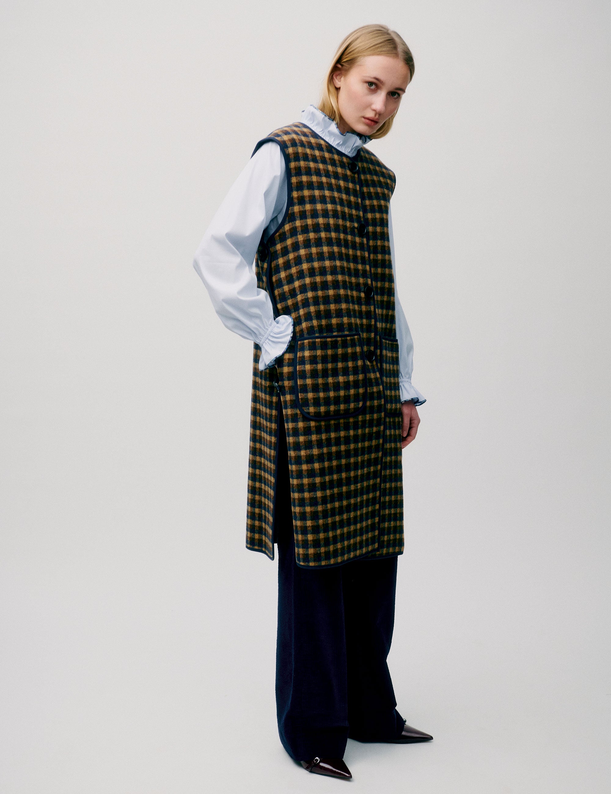 Woman in light blue shirt and long check patterned vest in yellow and black