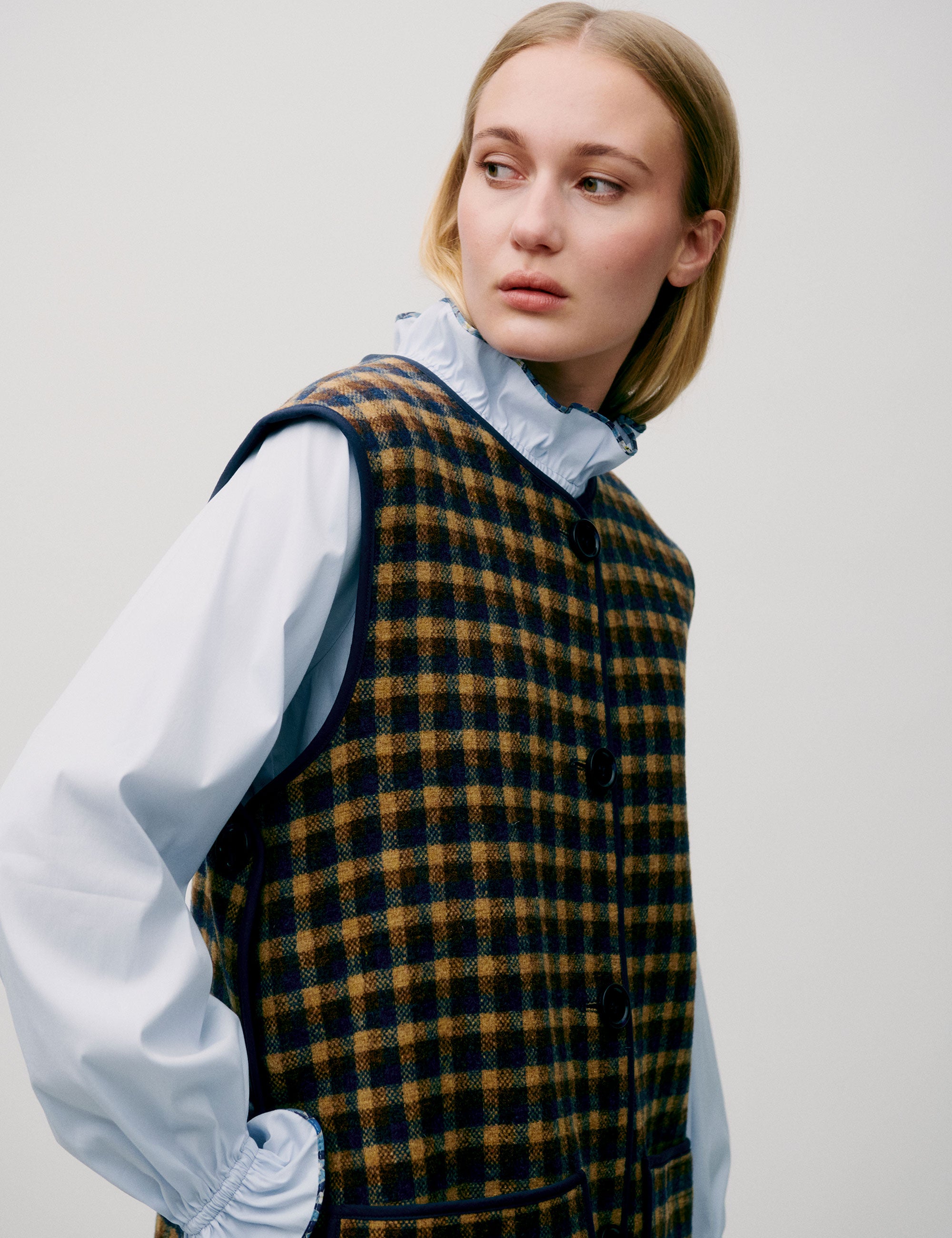 Woman in light blue shirt and long check patterned vest in yellow and black